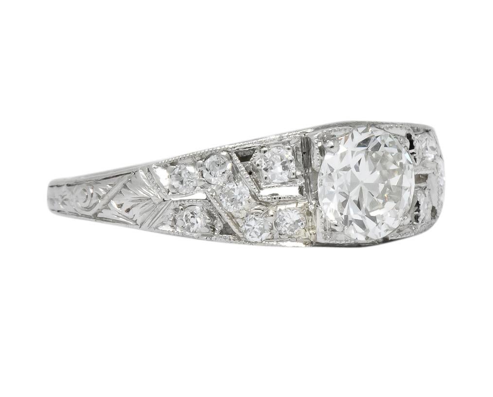 Centering, in a square form head, a transitional cut diamond weighing 0.77 carat, J color and VS1 clarity

Flanked by single cut diamonds bead set in a pierced millegrain crossed motif, weighing approximately 0.23 carat total, eye-clean and