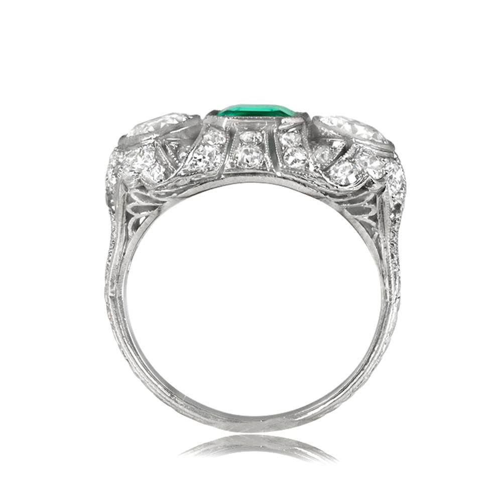 Antique platinum Edwardian ring features a 1.00 carat emerald-cut emerald, flanked by two bezel-set old European cut diamonds, and accented by a ribbon motif set with additional diamonds. Hand-engravings and fine milgrain add to its beauty. Crafted