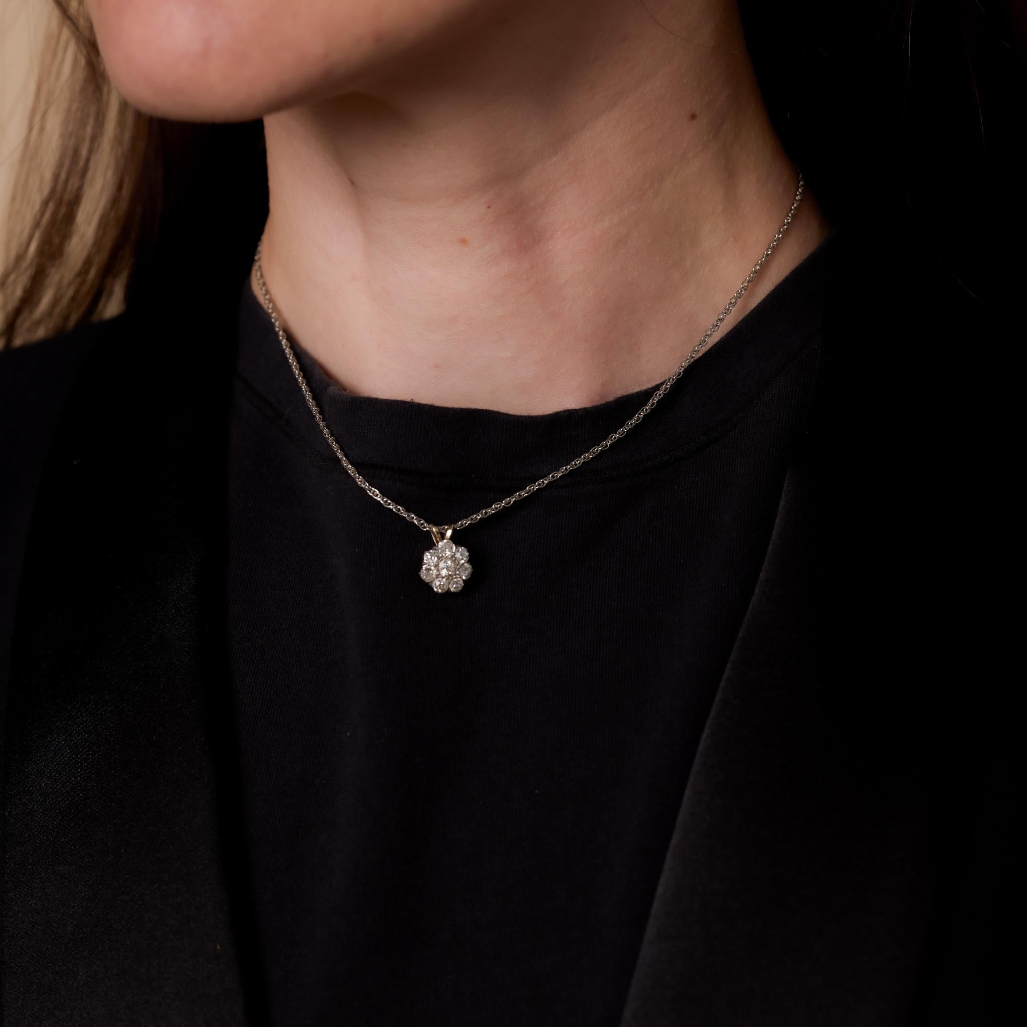 This Edwardian flower necklace features eight old European cut diamonds totaling 1.10 carats, H-I color, and VS-SI clarity. The pendant is crafted in 14k yellow gold and platinum with an added 14k white gold bail and chain from the 1990s. Measuring