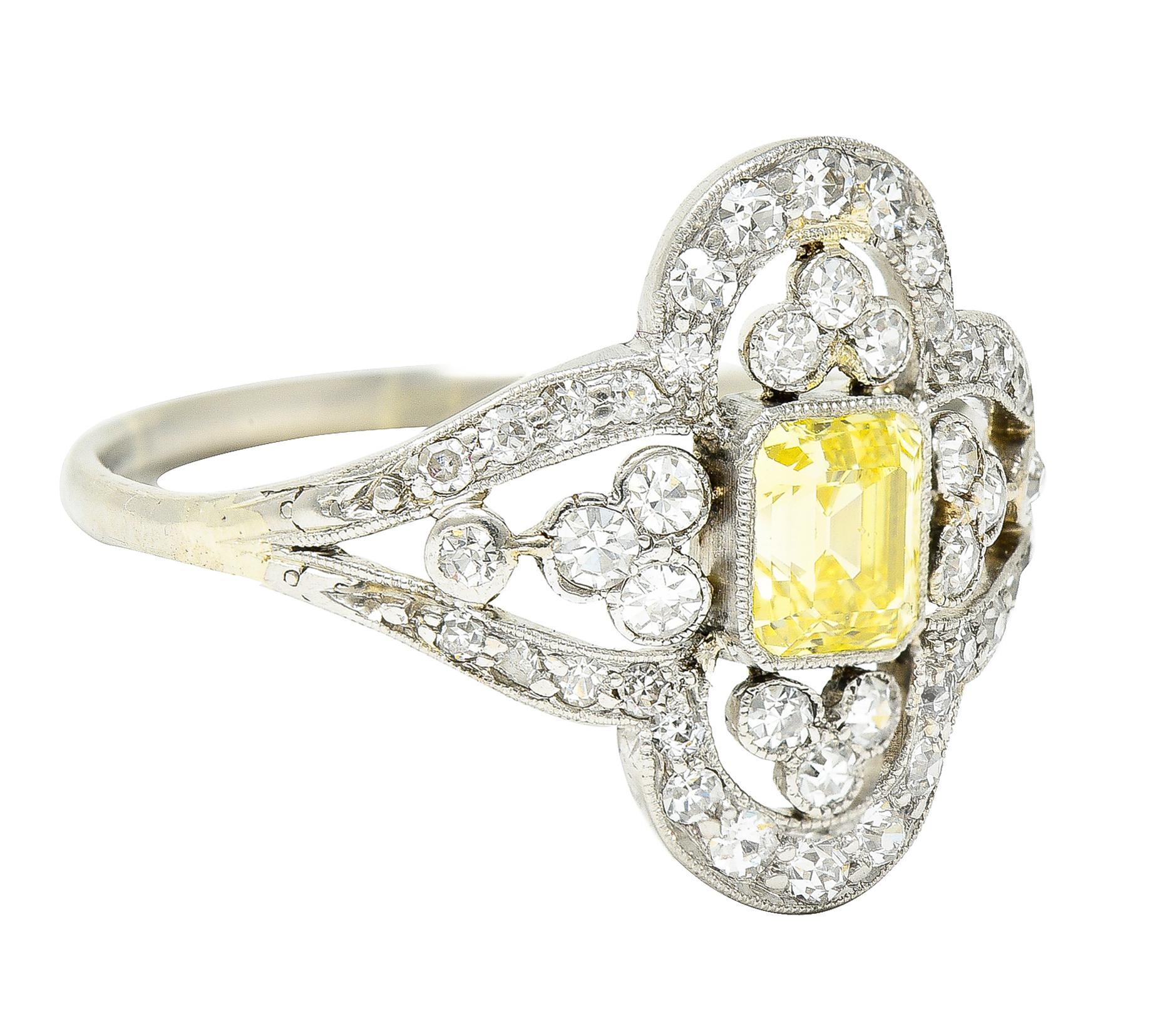 Centering an emerald cut diamond weighing approximately 0.62 carat total. Fancy light yellow in color with I1 clarity - bezel set with milgrain surround. Centered in a pierced quatrefoil motif with trefoil clusters at cardinal points. Featuring