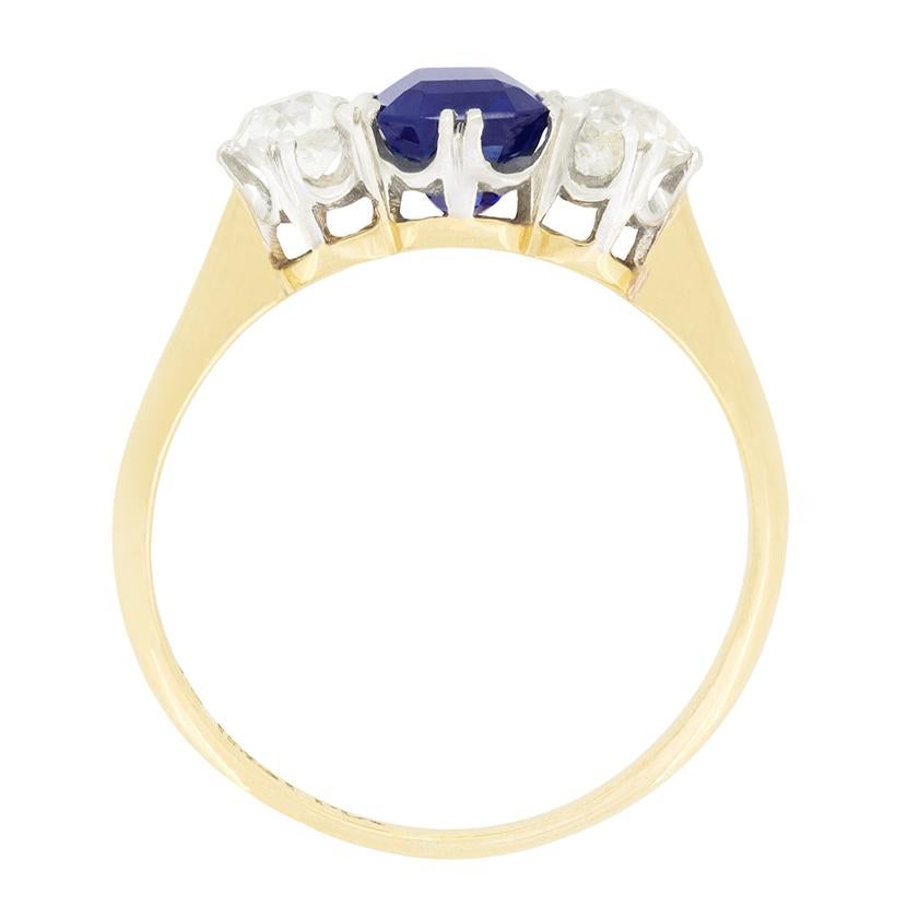 This beautiful trilogy ring features a central sapphire flanked by a pair of sparkling old cut diamonds. The intense blue sapphire is a natural stone, emerald cut and weighing 1.35 carat. The two diamonds weigh 0.30 carat each and match in quality