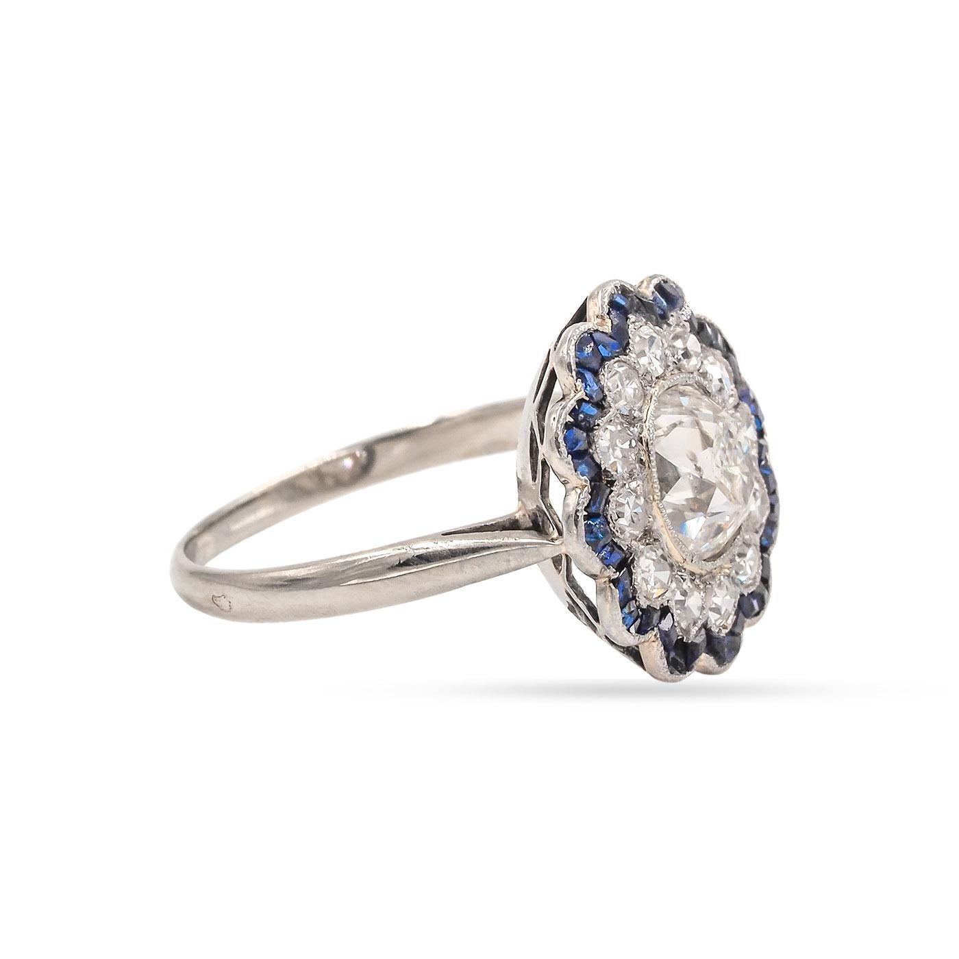Edwardian era 1.39 Carat Old Mine Cut Diamond and Blue Sapphire Cluster Engagement Ring composed of 18k white gold. The center stone Old Mine Cushion Cut is GIA certified J color & SI1 clarity. Surrounded by a halo of 12 Single Cut diamonds weighing