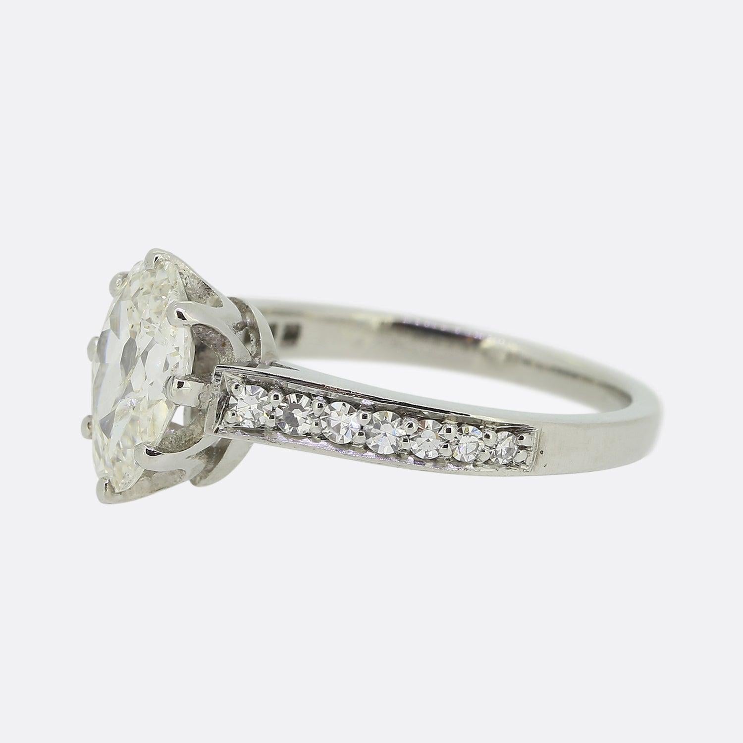 Here we have a wonderfully crafted diamond engagement ring. At the centre of the face we find an 1.40ct old pear shaped diamond which sits slightly risen in an eight clawed mount. The focal stone is flanked on either shoulder by a single row of