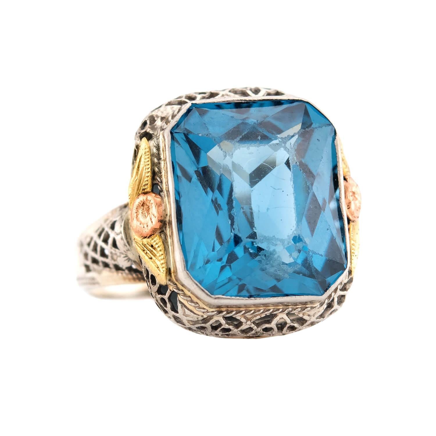 Un hermoso e inusual anillo de topacio azul de la época eduardiana (ca. década de 1910). Esta preciosa pieza está hecha de oro blanco, rosa y amarillo de 14 quilates y lleva un topacio azul talla esmeralda engastado en el centro. El topacio azul