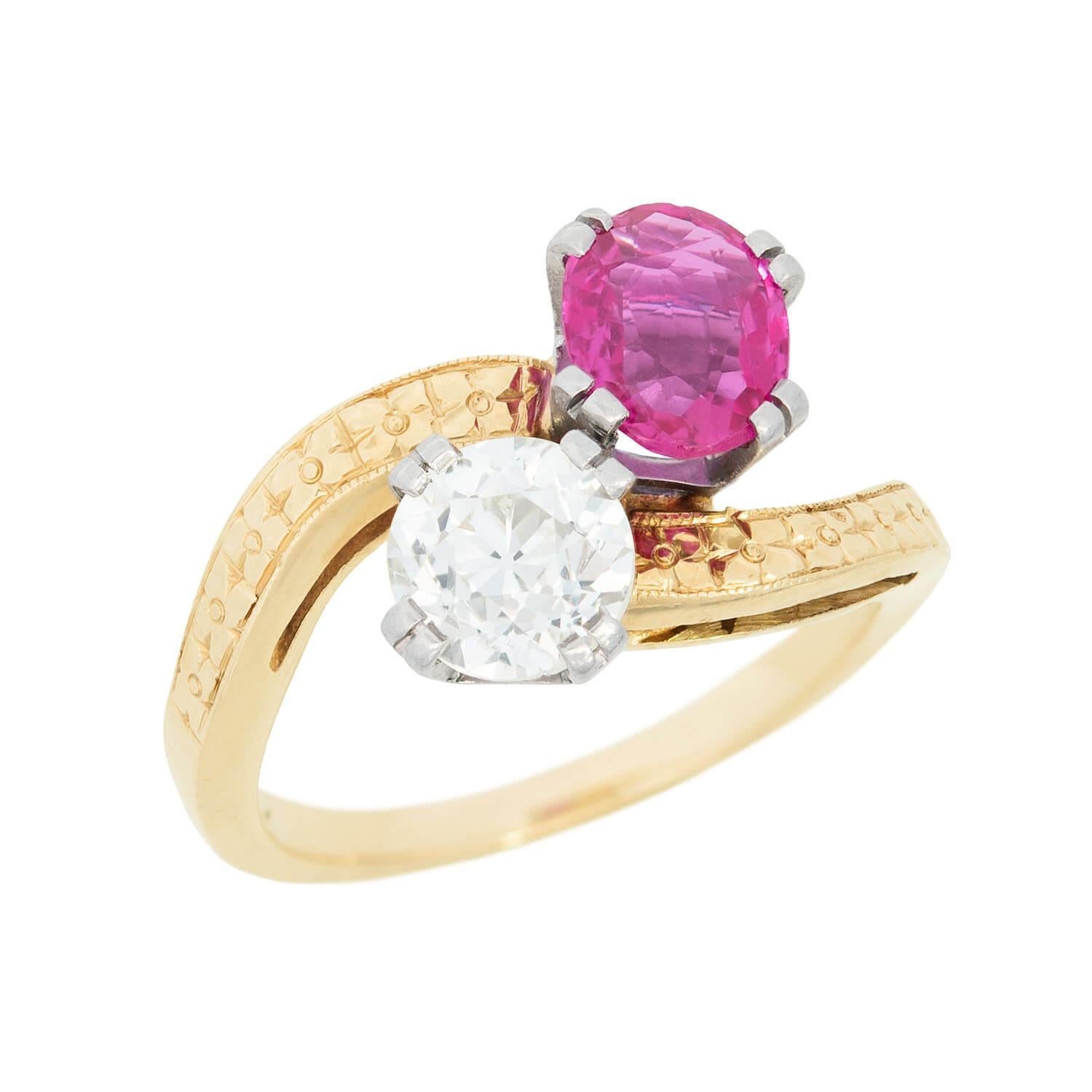 A stunning and unusual diamond and ruby bypass ring from the Edwardian (ca1910) era! Crafted in 14k yellow gold and platinum, the piece features a sparkling old mine cut diamond and vibrant oval cut ruby nestled together at the center, forming a