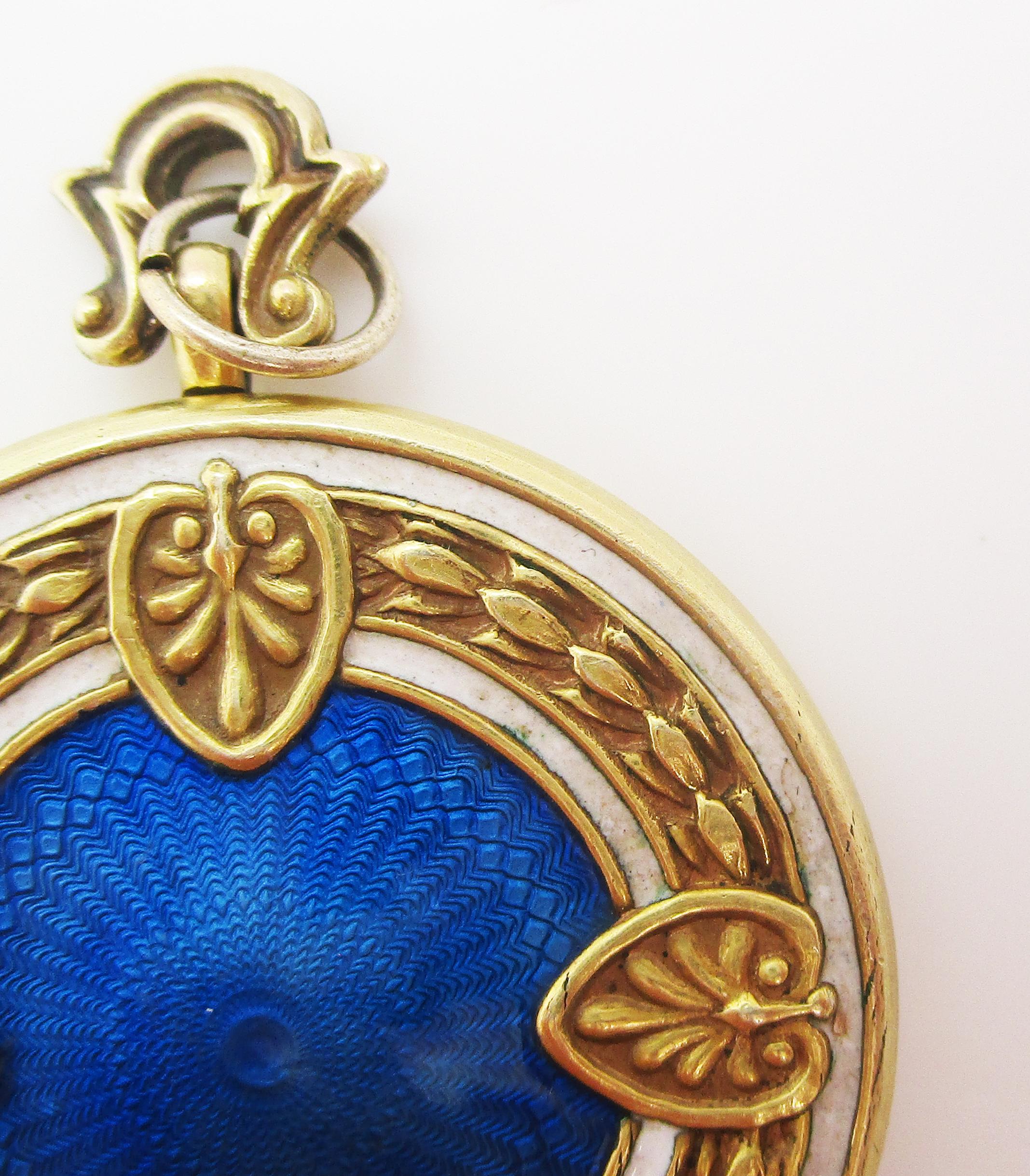 This is a gorgeous Edwardian two photo locket in 14k yellow gold featuring a stunning guilloche enamel front! 
The center of the front of the locket is a round field of deep royal blue guilloche enamel. It is framed with a white border, then another