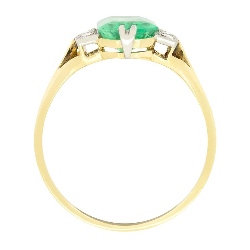 Completely unique in its design, this Edwardian ring centres around a 1.50 carat natural emerald. The shallow stone weighs 1.50 carat presents much larger on the finger. Set into platinum claws, the stone is flanked by a trio of eight cut diamonds,