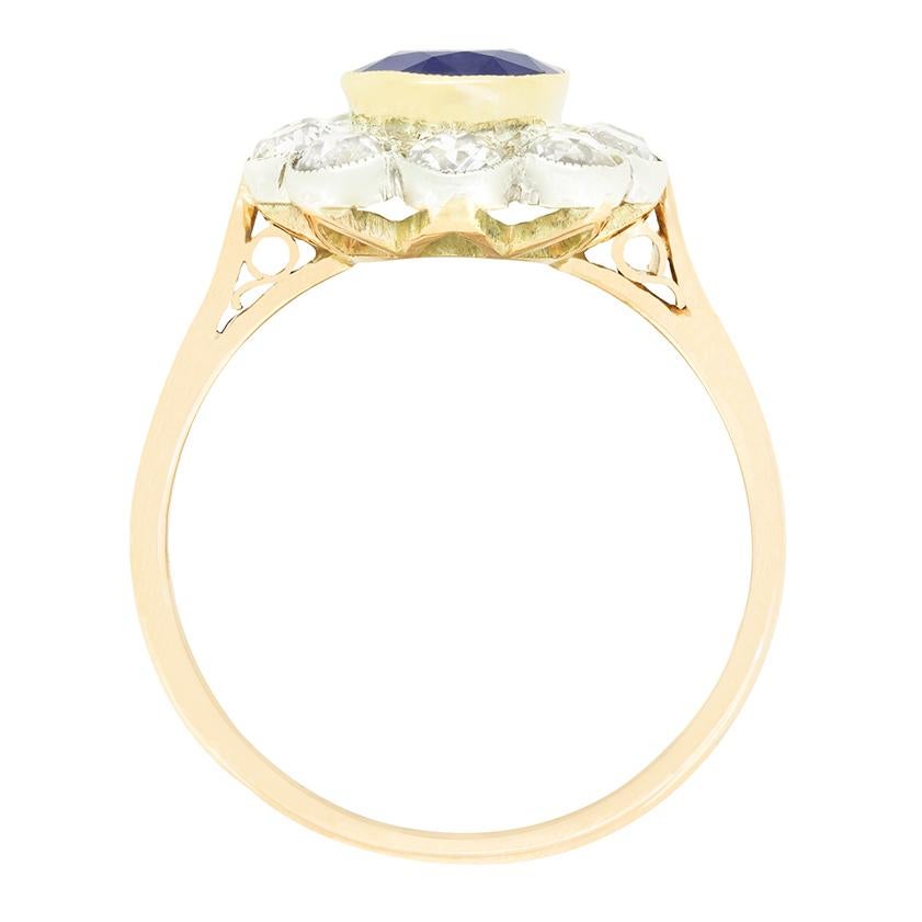 Cette magnifique bague à grappes date des années 1910. En son cœur se trouve un impressionnant 1,50 carat,  saphir bleu naturel. Le saphir est une pierre non chauffée, taillée en forme ovale et sertie dans de l'or jaune 18 carats. Le saphir est