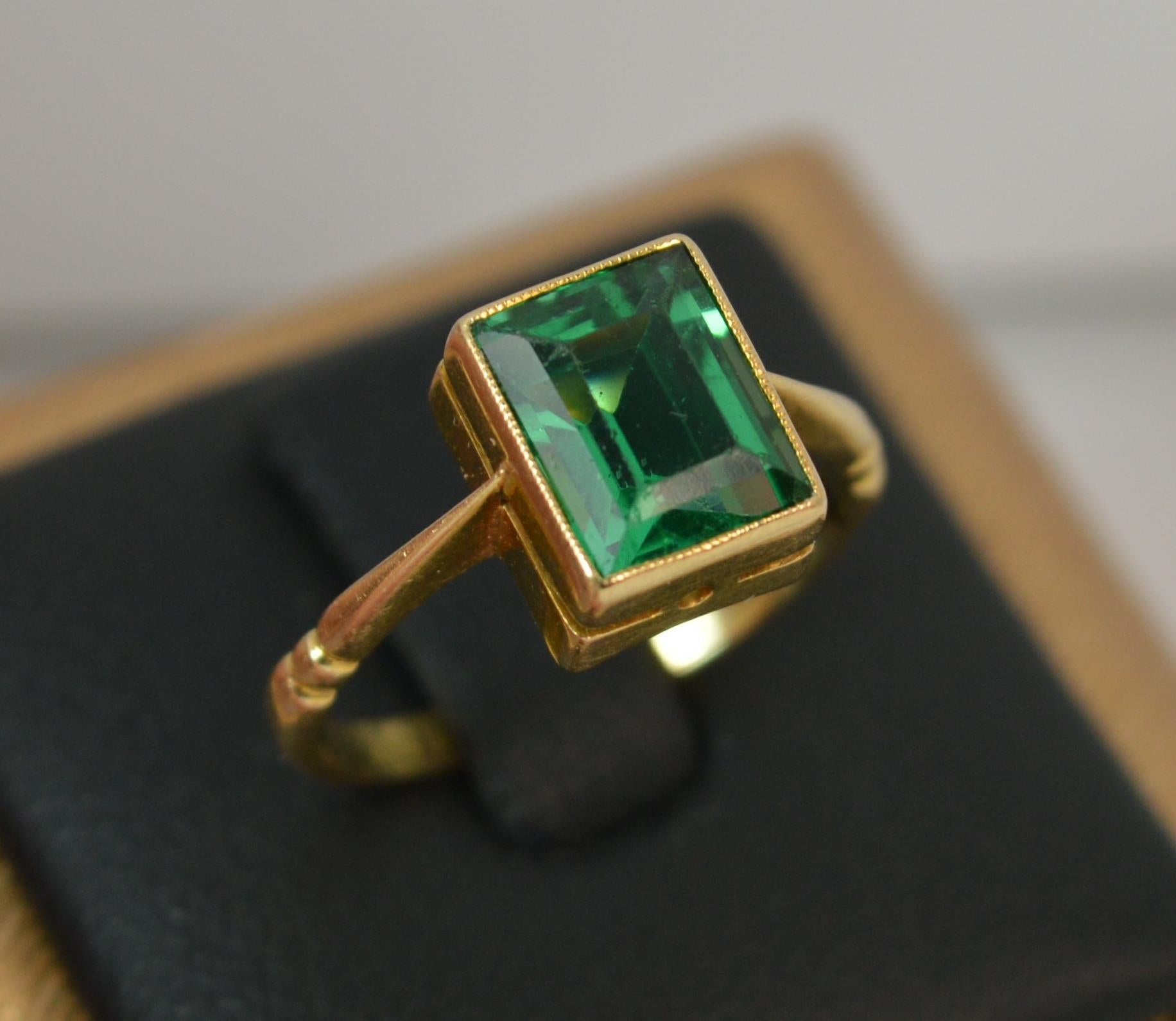 An Edwardian era 18 carat yellow gold and green stone solitaire ring.
Size i 1/2 UK, 4 1/2 US.
7.7mm x 6.2mm head.

2.1 grams. Set with an emerald cut green paste stone in fine grain bezel setting.

Light general wear only.