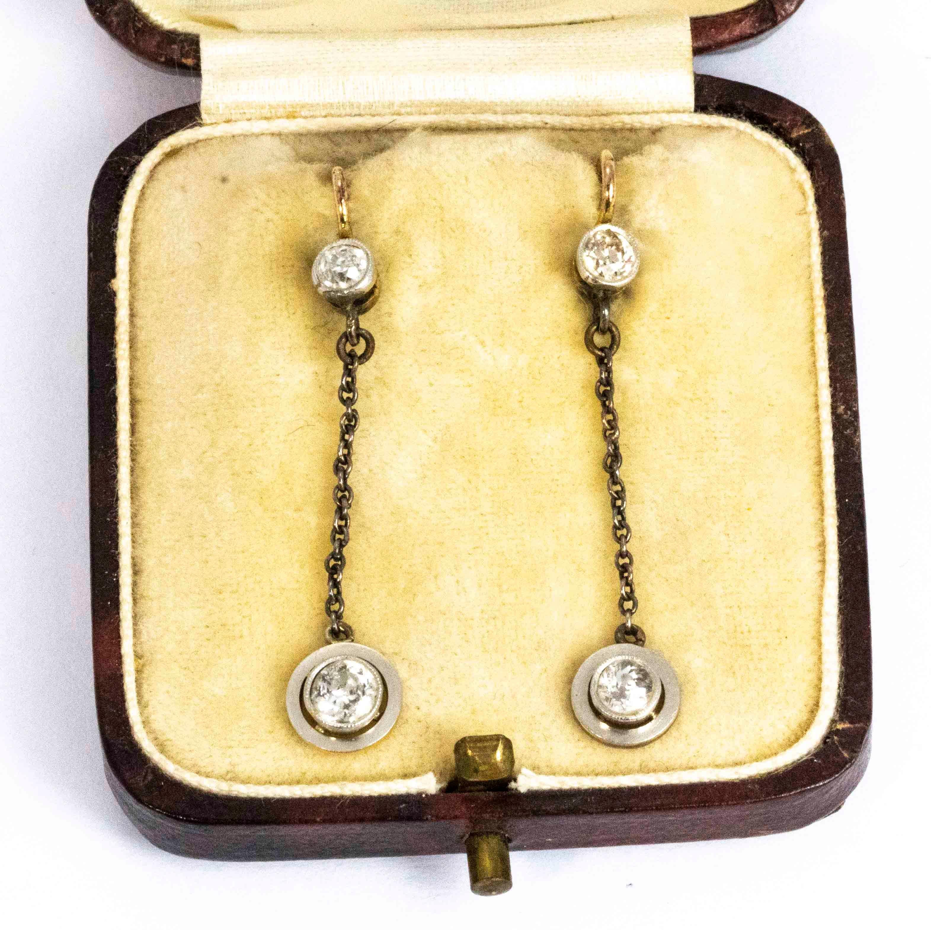 An exquisite pair of antique dangle earrings from the Edwardian period. Each earring starts with a stunning 18 point old European cut white diamond with a hooked back. Hanging below on an elegant chain sit 25 point diamonds in beautiful white gold