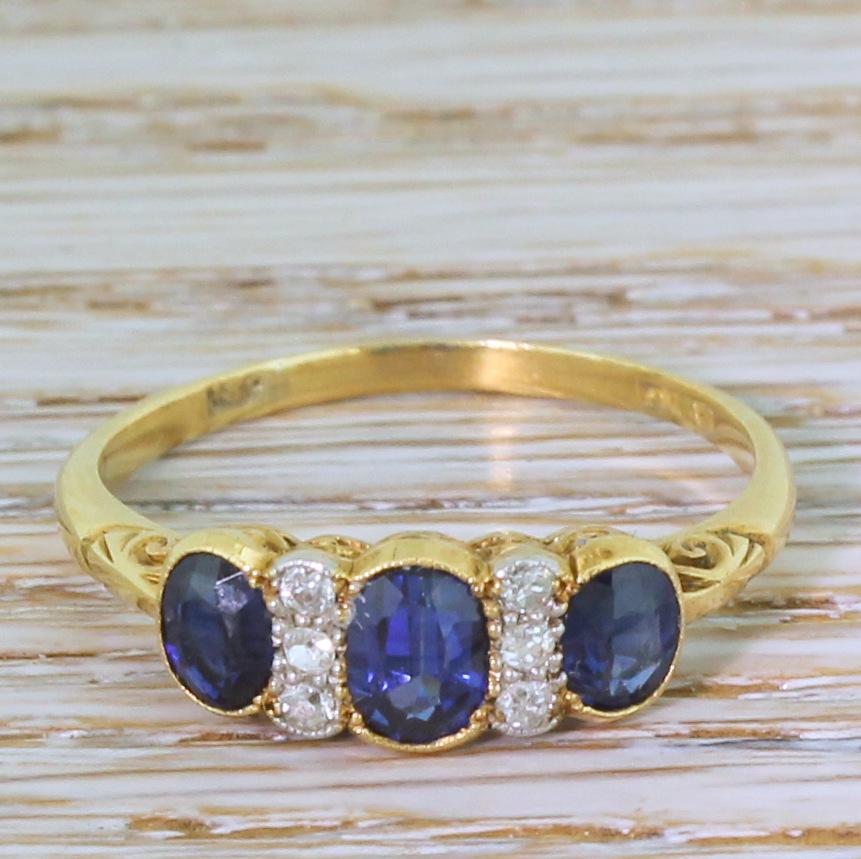 A wonderfully pretty antique sapphire ring. The trio of natural sapphires display a rich and bright blue, and are rubover set in milgrained yellow gold. Two sets of three old cut diamonds, set in platinum, are interspaced between the sapphires
