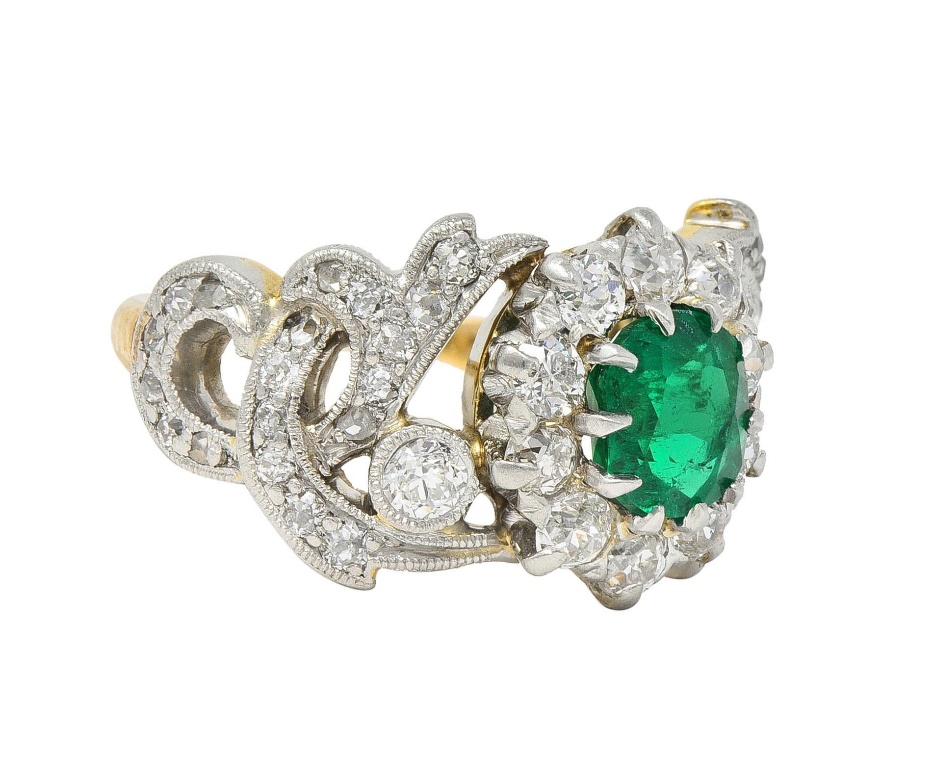 Centering a cushion cut emerald weighing approximately 0.81 carat - transparent medium green
Set with platinum talon prongs with a halo surround of prong set old European cut diamonds
Flanked by pierced and platinum-topped scrolling volute motif