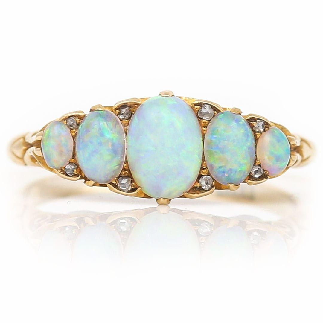 A fabulous Edwardian 18k yellow gold five stone opal ring, highlighted with eight diamond chips, hand crafted circa 1910. A traditional setting with carved claw detail, the graduated oval opals have a wondrous play of colour, with blue, pink and