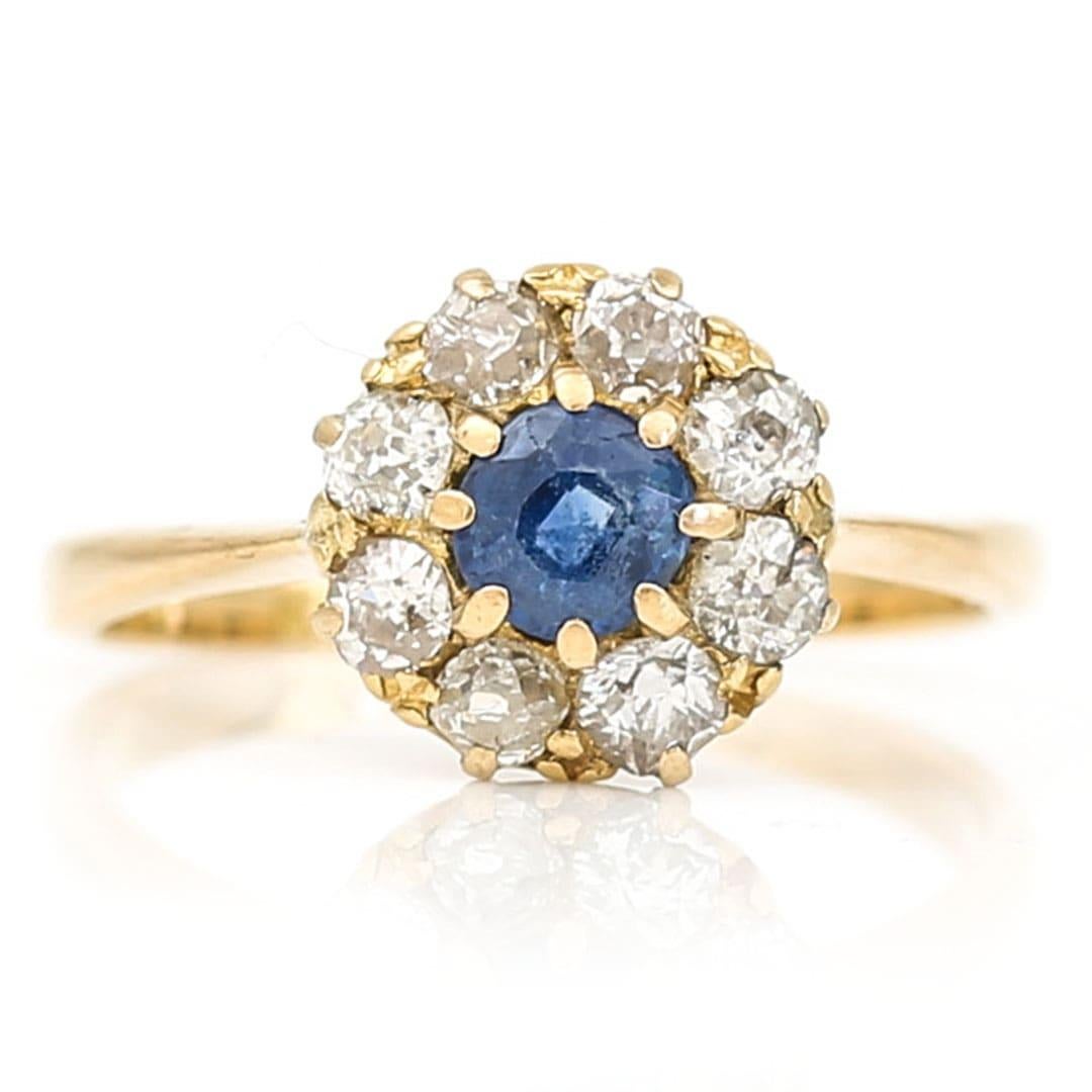 A timeless design this 18ct yellow gold sapphire and diamond halo cluster ring is set with a approx 0.30ct oval, pale blue sapphire around which a cluster of 0.30ct of old cut diamonds are claw set. The setting of the diamonds remind us of a