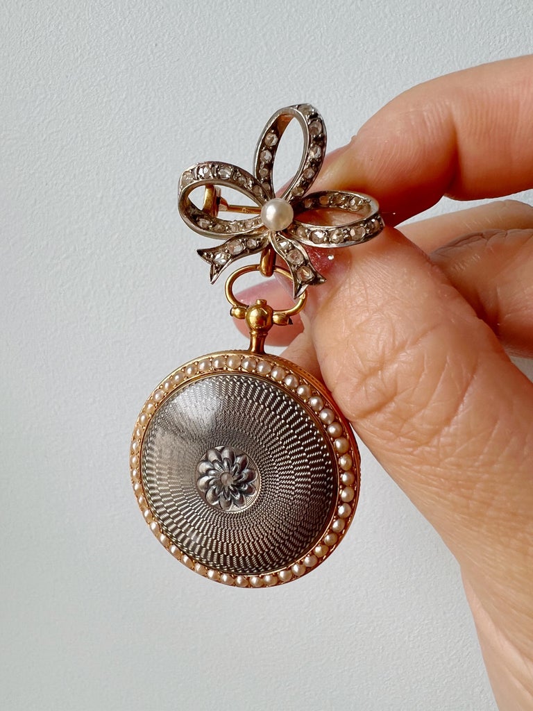 Magnificent is the first word comes to mind when looking at this Edwardian era 18K solid gold pocket watch pendant. It has an elegant bluish gray guilloche enameling and is framed with the gentle natural seed pearls on both sides. The center of the