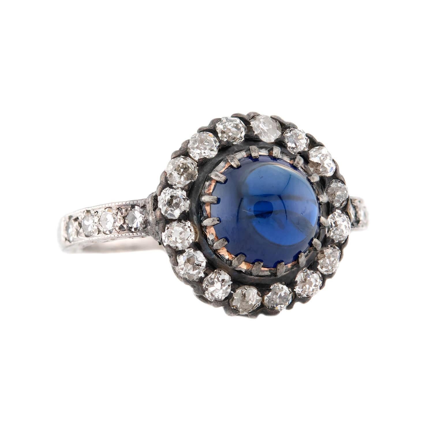 An exquisite sapphire and diamond ring from the Edwardian (ca1910s) era! Crafted in 18k white gold and platinum, this ring features a central prong-set 1.20ct sapphire cabochon. The cabochon is a no heat Ceylon, and displays a marvelous deep blue