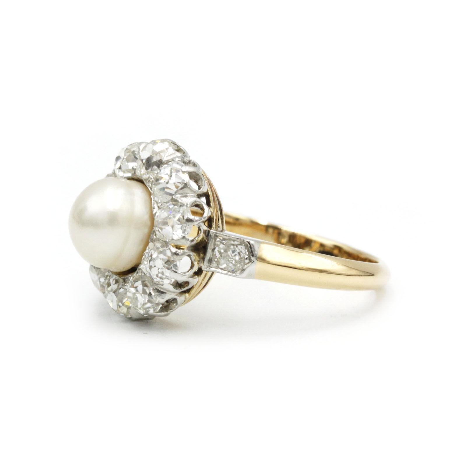 A quintessential example of early 20th-century refinement, this Edwardian cluster ring is crafted in 18K yellow gold and platinum (hallmarked “750” and “950”), centering on a lustrous round pearl framed by a halo of twelve old European–cut diamonds.
