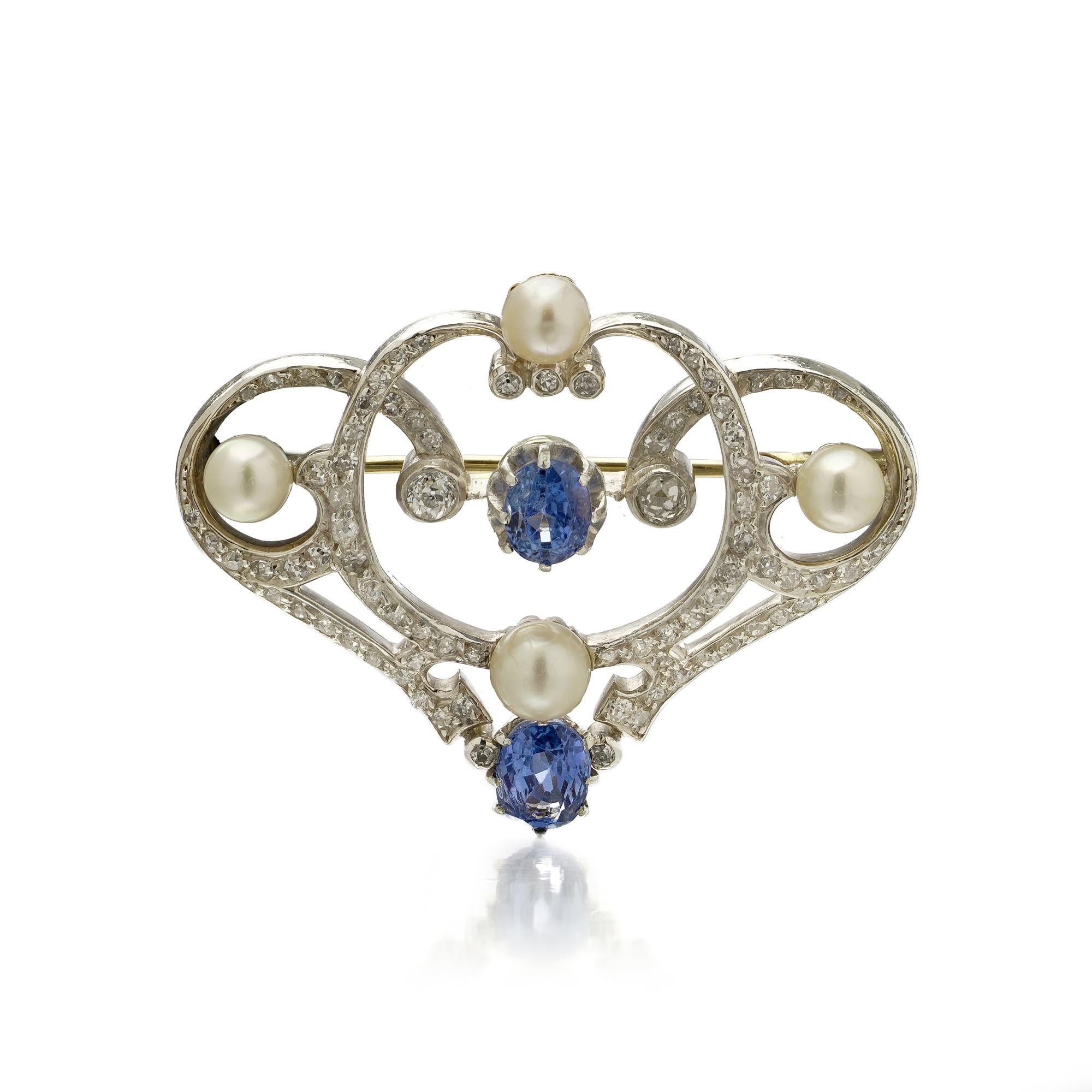 Broche édouardienne finement travaillée en or jaune 18 carats avec sertissage en platine. Le motif ajouré de la volute est pavé de 83 diamants de taille ronde, brillante et simple. Il est orné de deux saphirs naturels de Ceylan à facettes ovales,