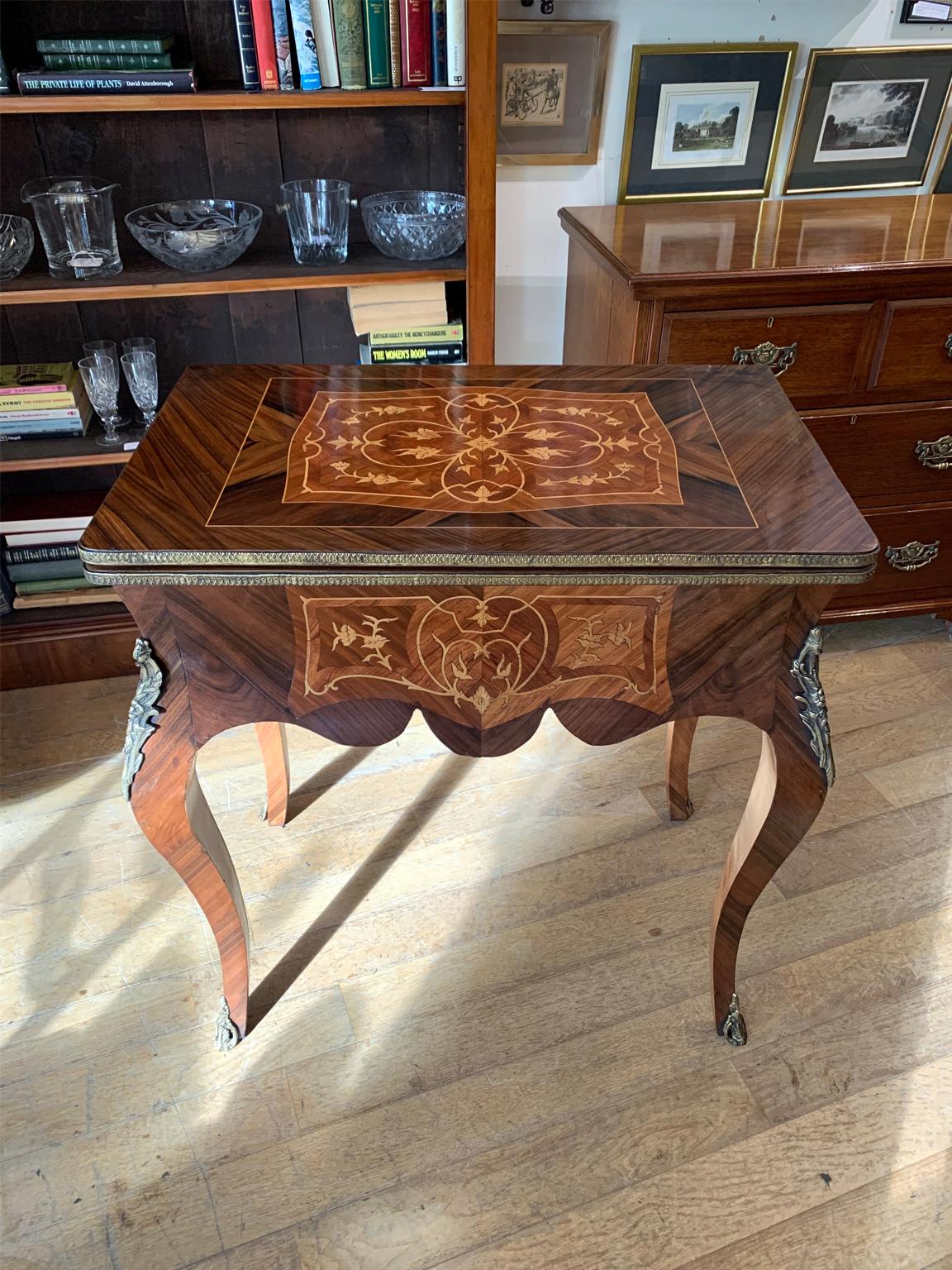 An Edwardian / 1920’s French Inlaid Kingwood Card Table with green baize interior and fitted metal mounts throughout. Raised upon cabriole legs with scroll feet, the top swivels open to become a card table. Circa: 1900 / 1920.



