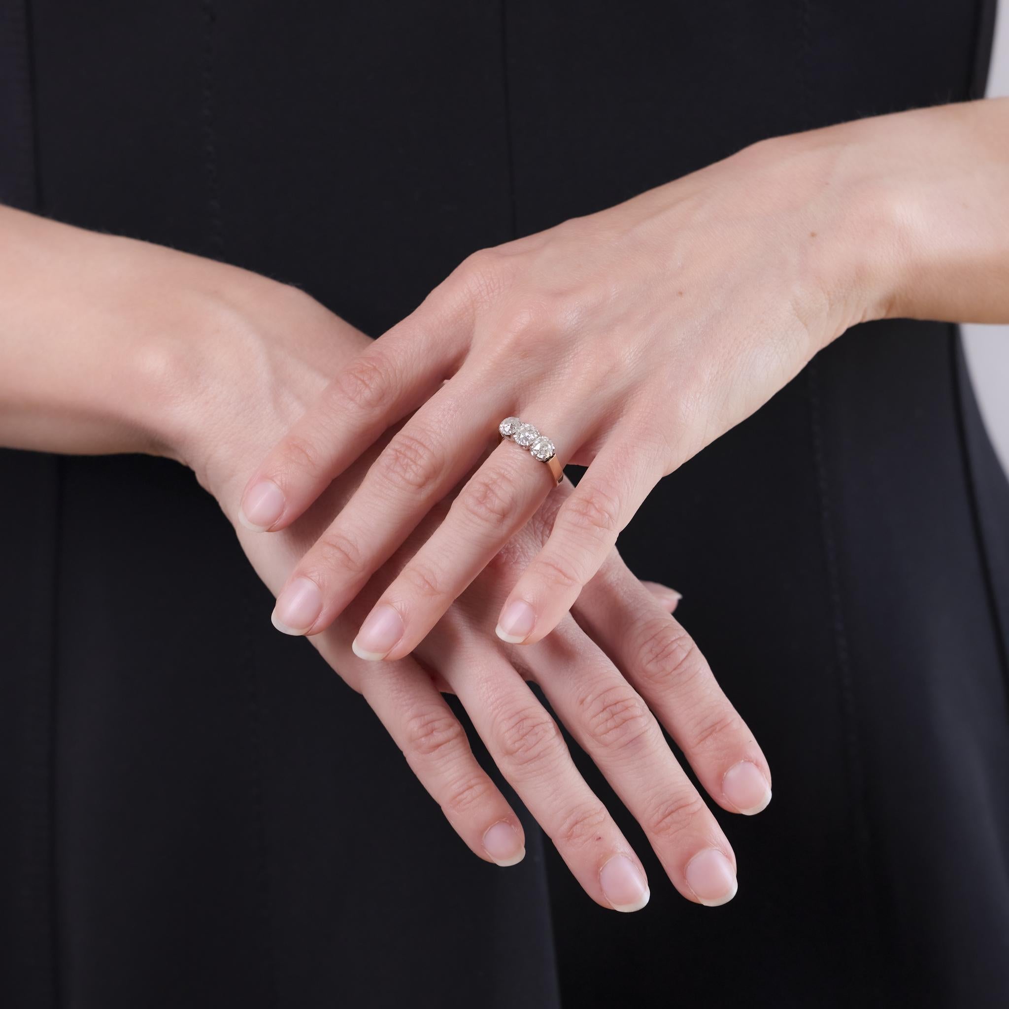 This Edwardian ring from the 1910s is crafted in 18k yellow gold with a platinum top and features three old mine cut diamonds totaling approximately 2 carats. The diamonds are graded G color and SI clarity, offering antique brilliance and a softly