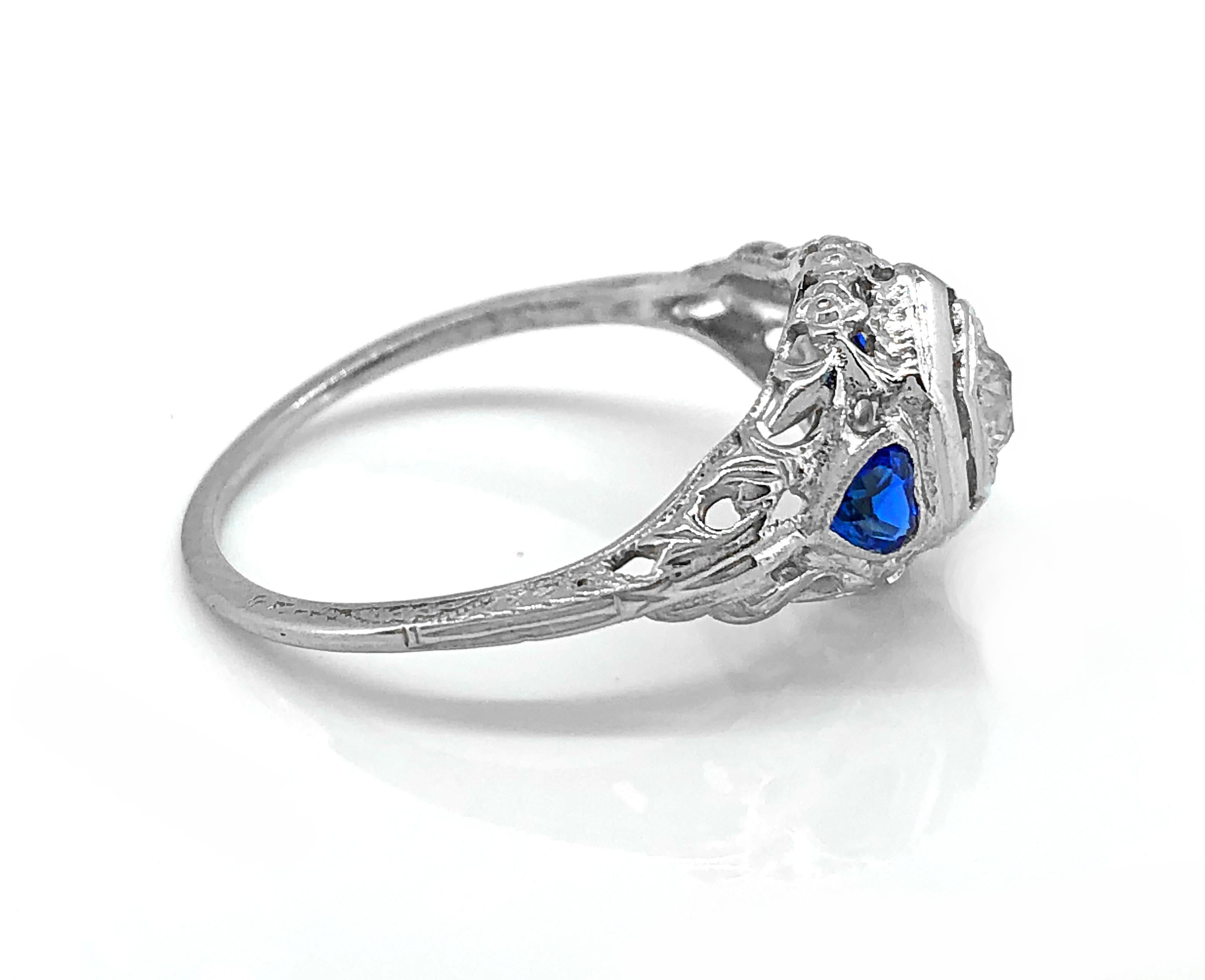 A sweet Edwardian diamond and sapphire Antique engagement ring featuring approximately .20ct. Apx. T.W. of European cut diamonds with VS2 clarity and H color and approximately .40ct. Apx. T.W. of synthetic heart shaped blue sapphires. The beautiful