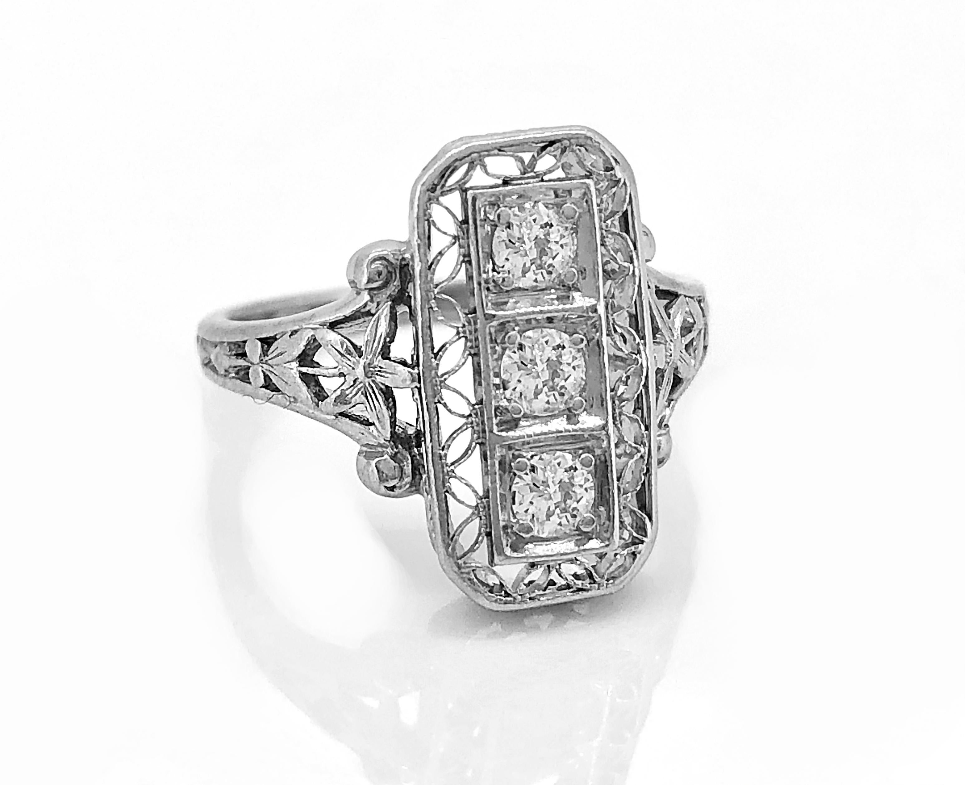 A delicately filigreed Edwardian antique fashion ring crafted in platinum that features 3 European cut diamonds that weight .20ct. apx. T.W. The head and gallery are artistically pierced and the shoulders are engraved with a flower at the top of the