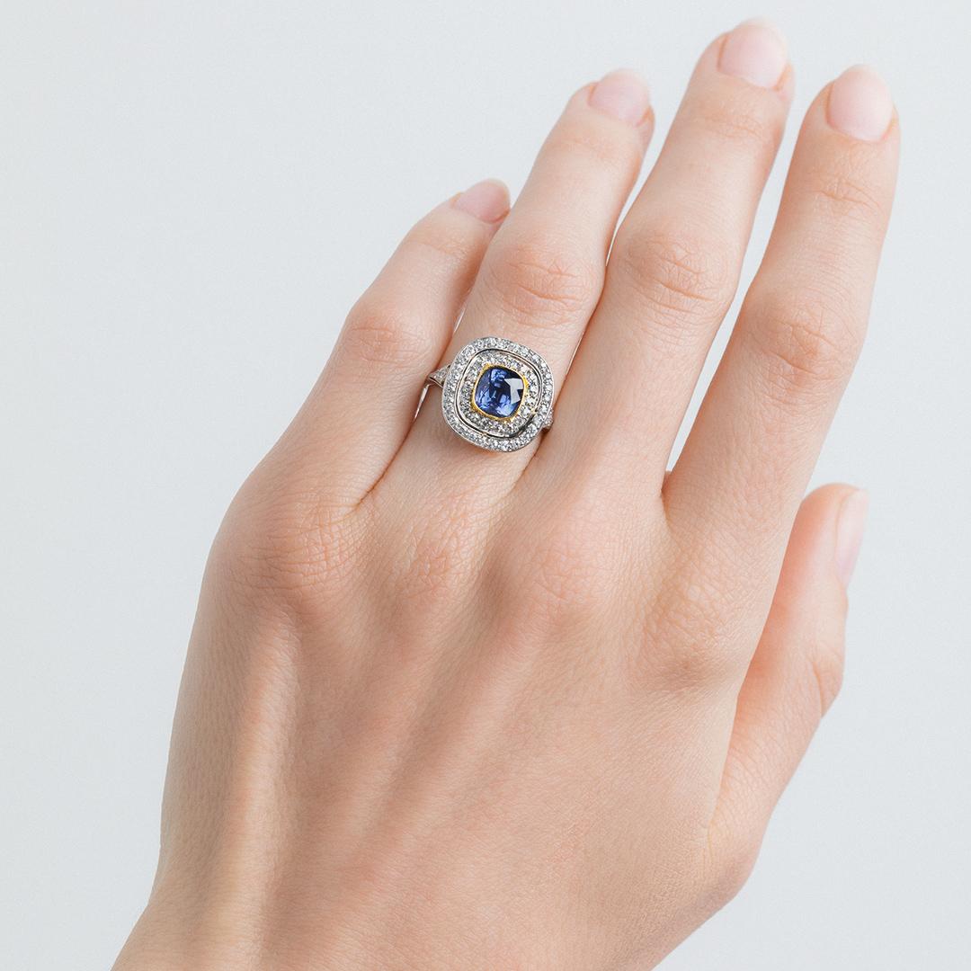 This is an impeccable and authentic Edwardian era (circa 1910) platinum and 18k yellow gold double halo ring. The ring centers a bezel set Cushion Cut sapphire gauged at 2.05ct and accompanied by a Guild Laboratories certificate stating the sapphire