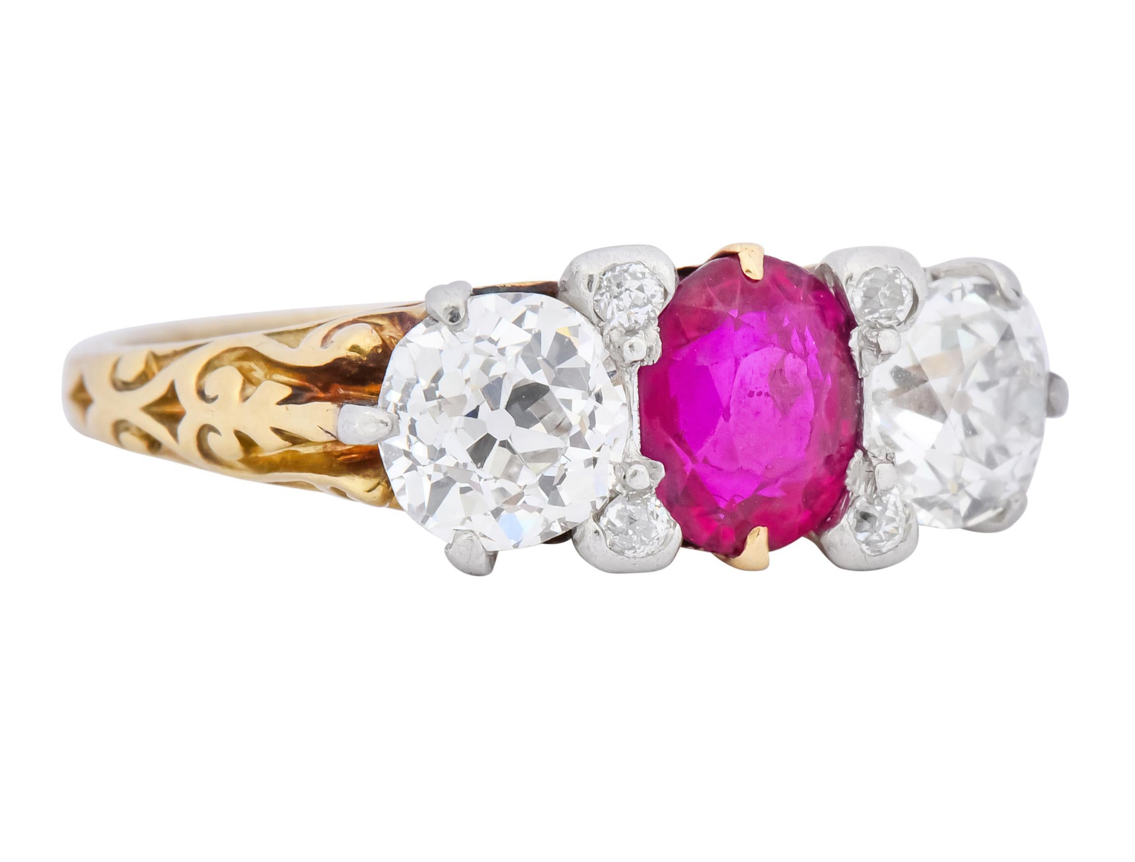 Three stone ring with platinum topped setting and scrolled yellow gold motif throughout shoulders and gallery

Centering an oval cut Burmese ruby, no heat, weighing approximately 1.00 carat, transparent and saturated in color

Flanked by two old