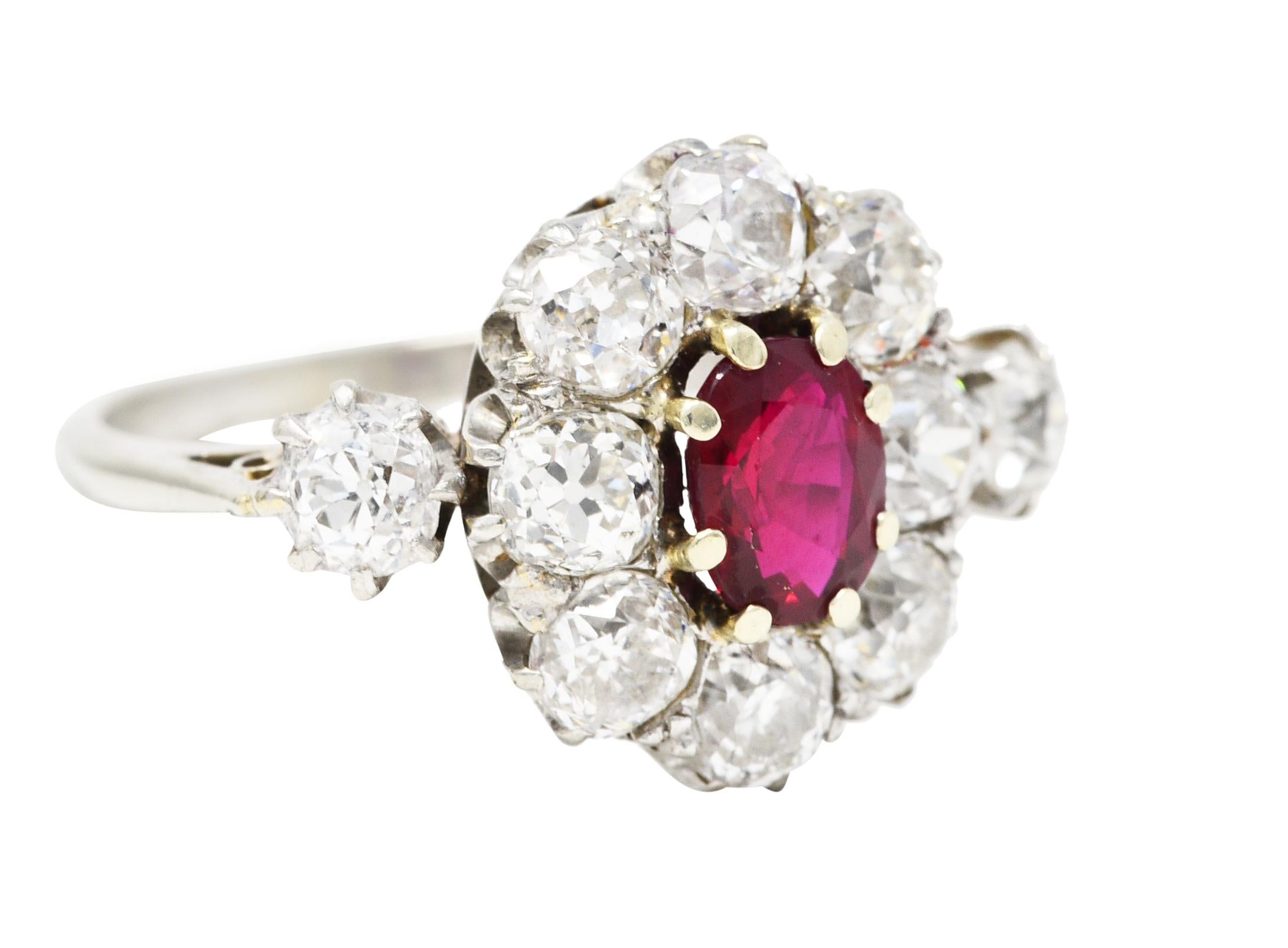 Cluster ring centers an oval cut ruby weighing approximately 0.70 carat. Eye clean with vivid red color then set with yellow gold prongs. Surrounded by a halo of old mine cut diamonds with two additional at each shoulder. Weighing collectively