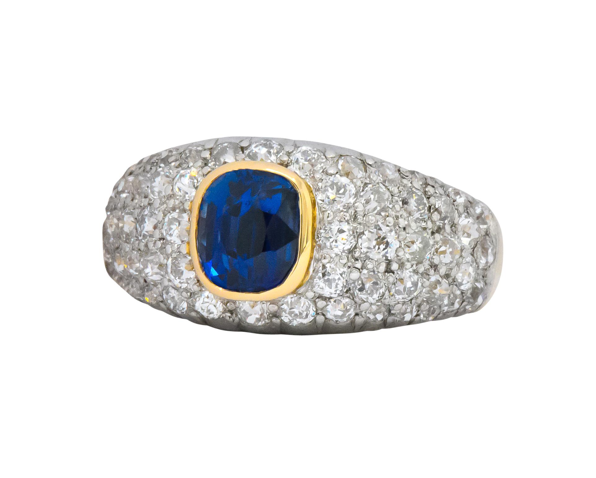 Band style ring centering a cushion cut sapphire weighing approximately 1.50 carats

Sapphire is bezel set in brightly polished gold and is transparent with striking royal blue coloring

Surrounded by pavé set round brilliant and Swiss cut diamonds