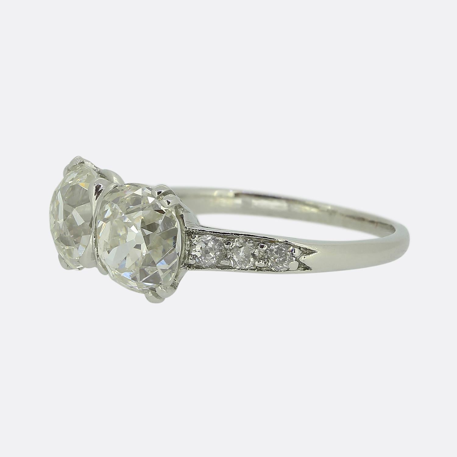 Here we have a delightful two-stone diamond ring taken from the Edwardian period. This antique piece showcases two round faceted chunky old cut diamonds, each sitting proud in a four clawed setting at the centre of the face. A trio of matching