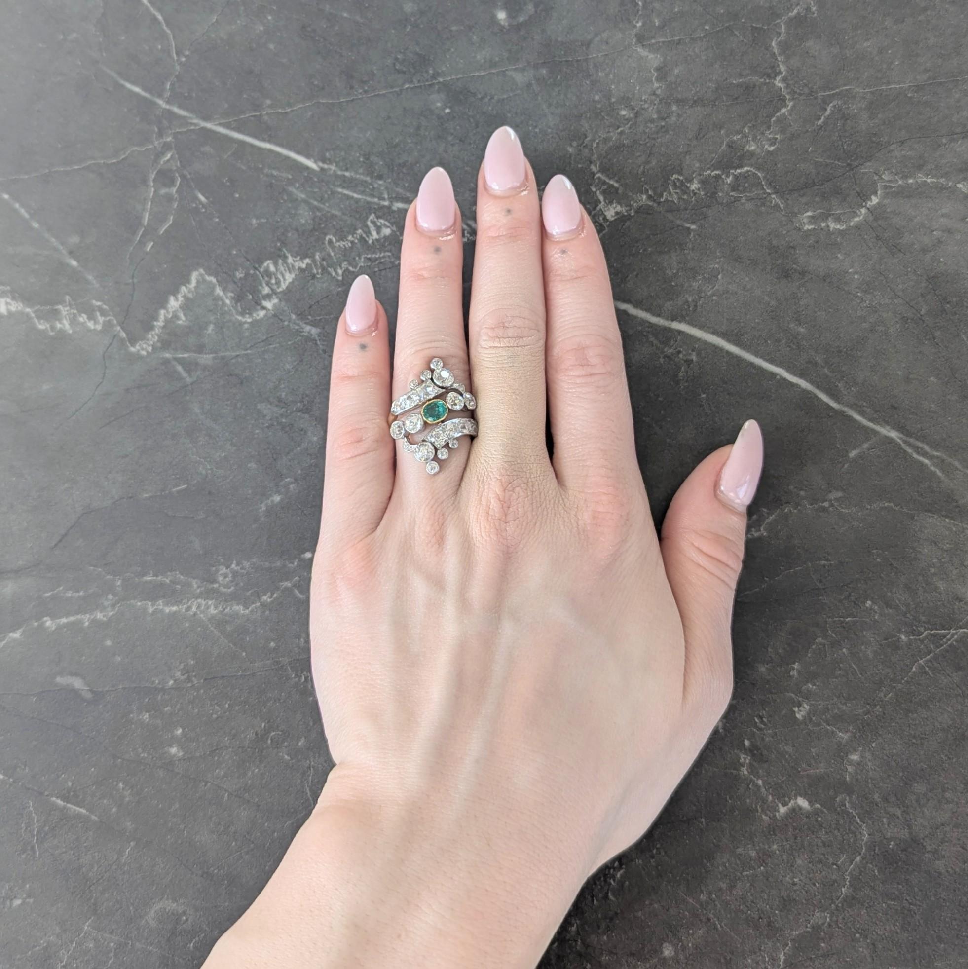 Centering a cushion cut emerald weighing approximately 0.45 carat total - transparent medium green in color
Bezel set in yellow gold and flanked by platinum-topped scrolling bypass style shoulders
Bead set with old European cut diamonds weighing