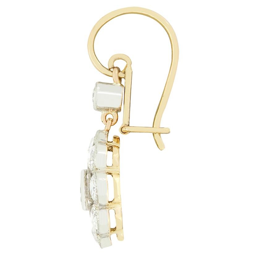 Dating back to the 1910s, this elegant pair of daisy drop earrings are entirely hand crafted. Each earring features a rub over set into platinum a central old cut diamond weighing 0.30 carat surrounded by a halo of nine 0.15 carat stone. An