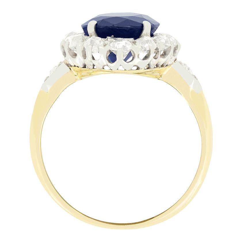 Un vibrante zafiro azul ocupa el centro, rodeado de brillantes diamantes talla antigua, en este anillo eduardiano en racimo. El zafiro calentado es una piedra de talla ovalada que pesa 3,75 quilates. Rodeando al zafiro, los diamantes suman un total