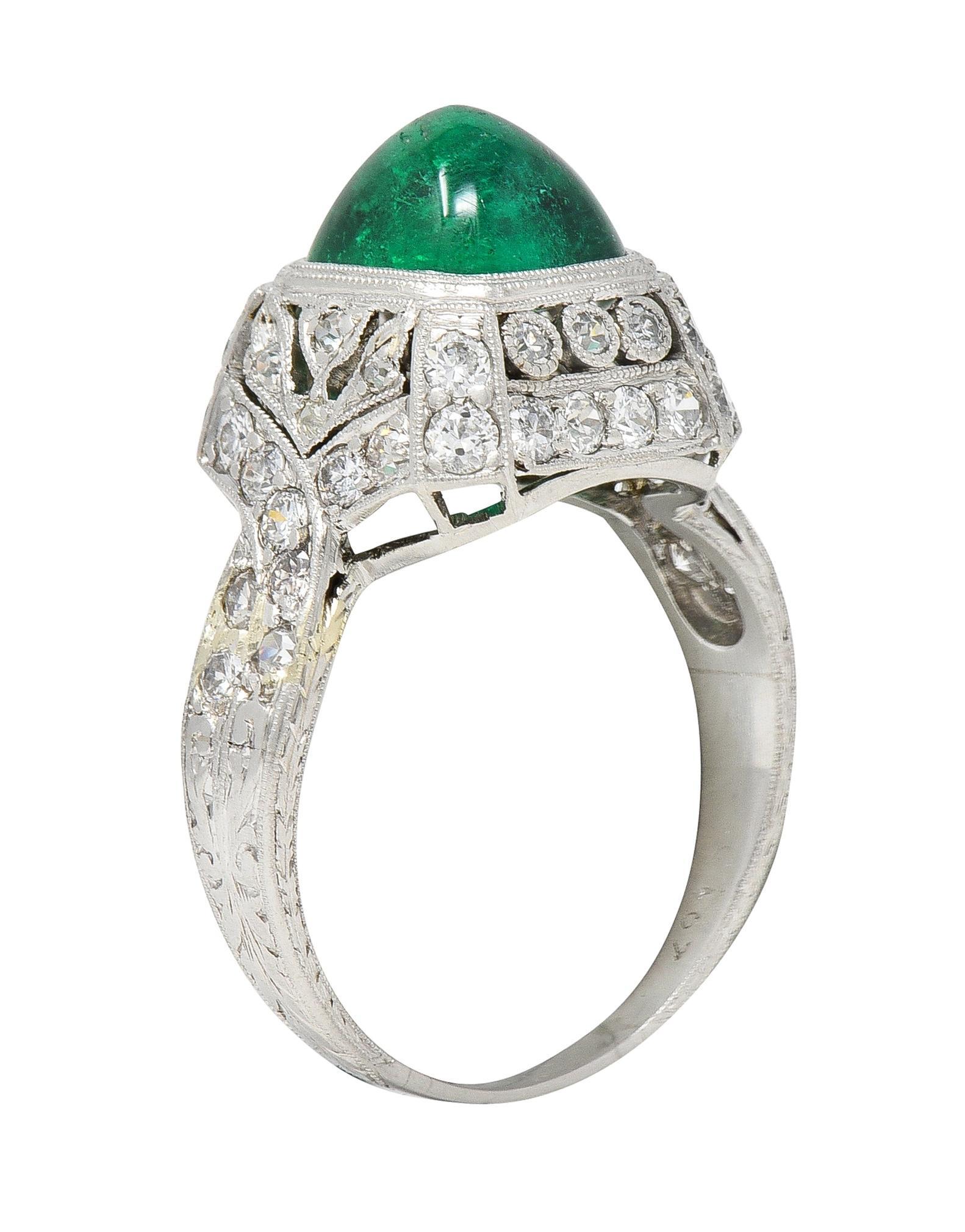 Centering a sugarloaf-shaped emerald cabochon weighing approximately 2.71 carats total 
Transparent vibrant medium green in color - bezel set in domed cushion-shaped surround 
Accented by pierced ribbon and tulip motifs set with single cut diamonds