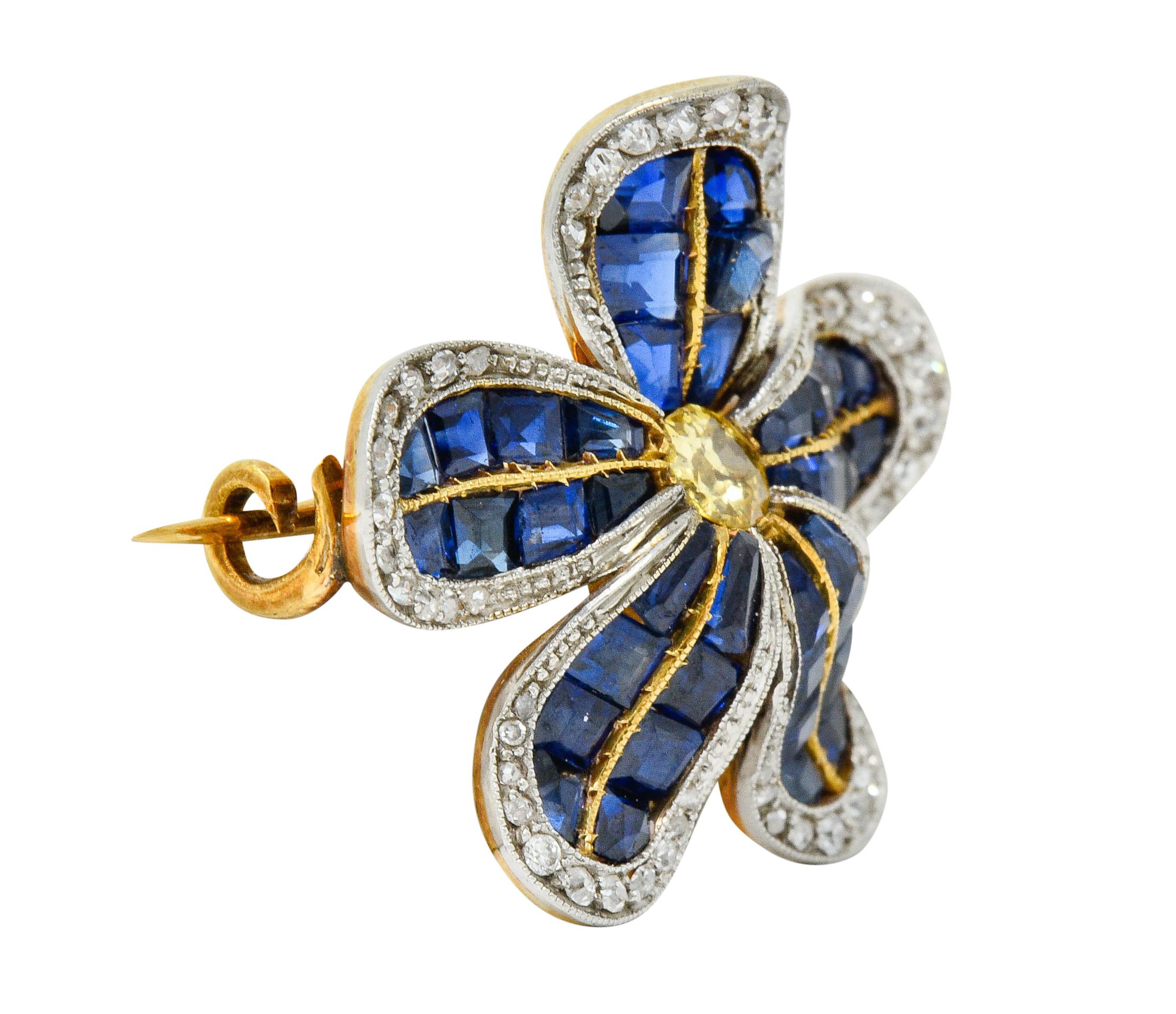Brooch is designed as a dynamically formed five petaled flower

Centering an old mine cut fancy colored diamond weighing approximately 0.22 carat
Fancy yellow in color with I clarity

Petals are invisibly set with calibrè cut sapphires weighing in