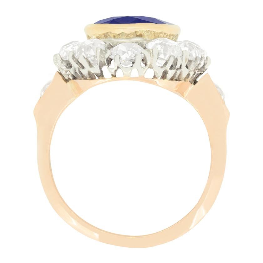 Questo anello a grappolo da capogiro risale al 1910. Al centro si trova un bellissimo zaffiro dal taglio ovale. La pietra da 4,80 carati è completamente naturale e non riscaldata ed è incastonata nell'oro giallo da 18 carati a contrasto. Lo zaffiro