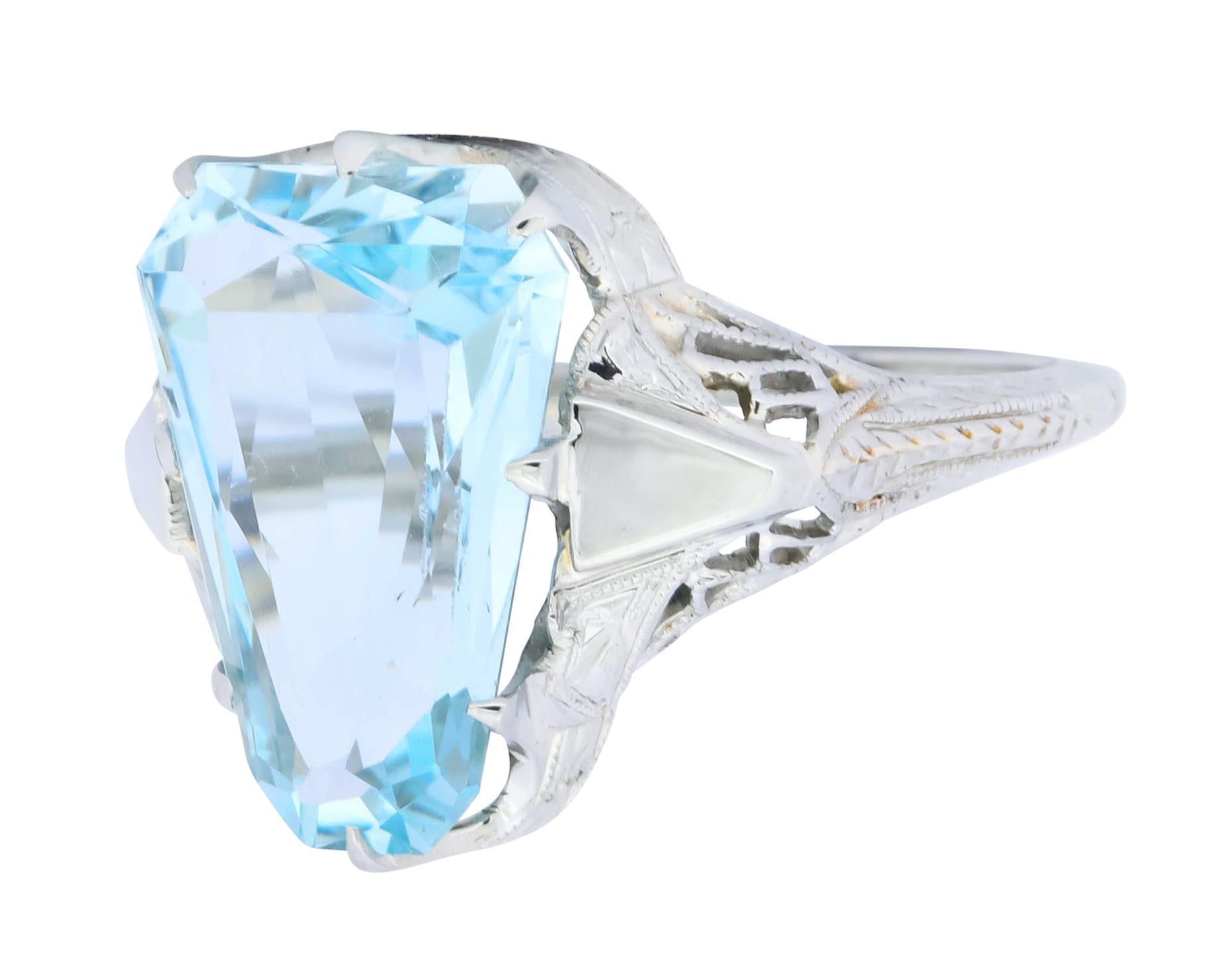 Centering a fancy cut aquamarine weighing 4.90 carat total, transparent and a very slightly greenish light blue color

Stone shape mimicked as highly polished tapered wedge shoulder motif

With pierced decorative mounting and engraved floral and