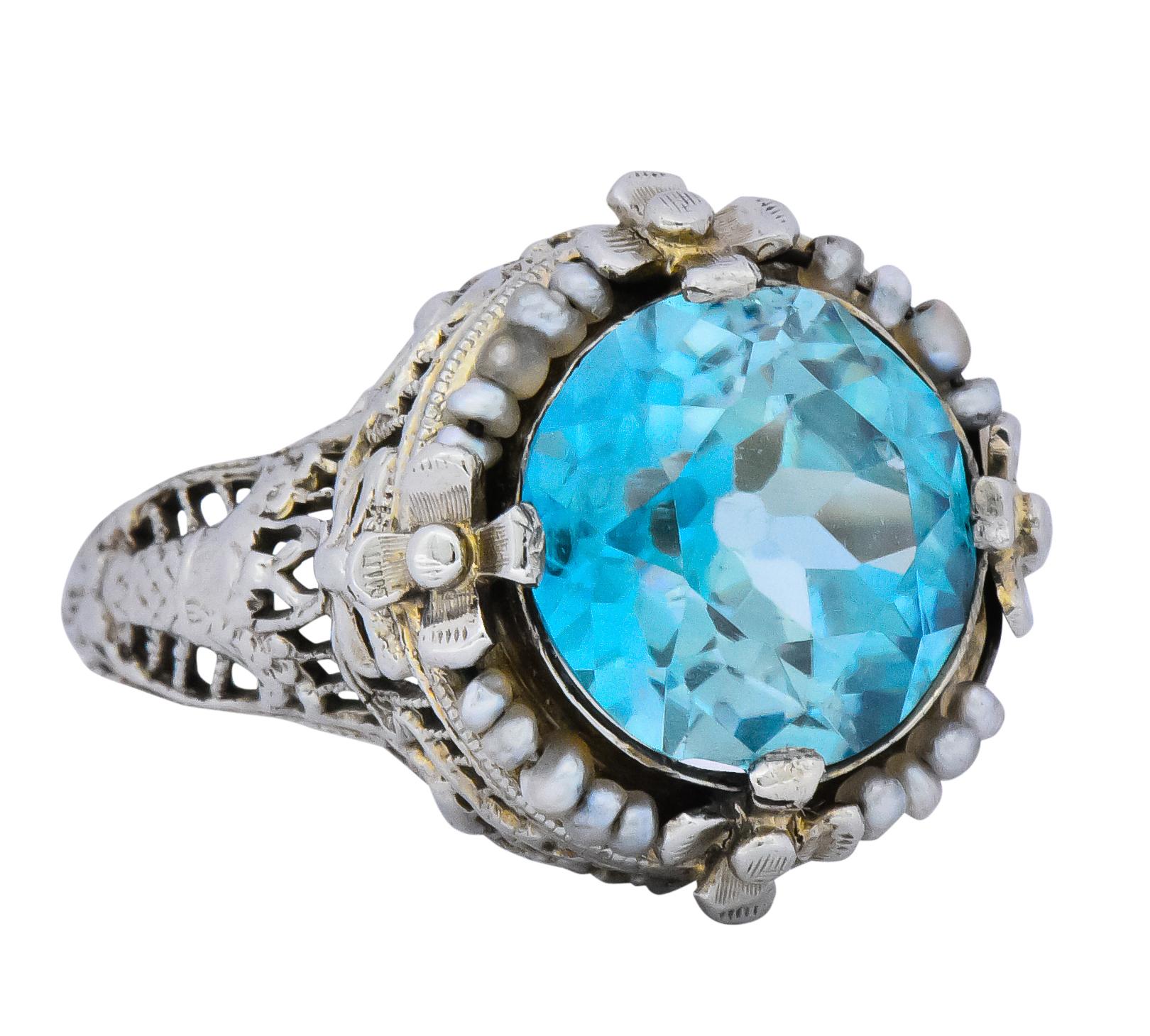 Centering a mixed European cut blue zircon weighing approximately 5.00 carats, transparent medium greenish-blue

Surrounded by beaded seed pearls and four flower stations

With linear pierced gallery featuring bow and bouquet motif on shoulders and