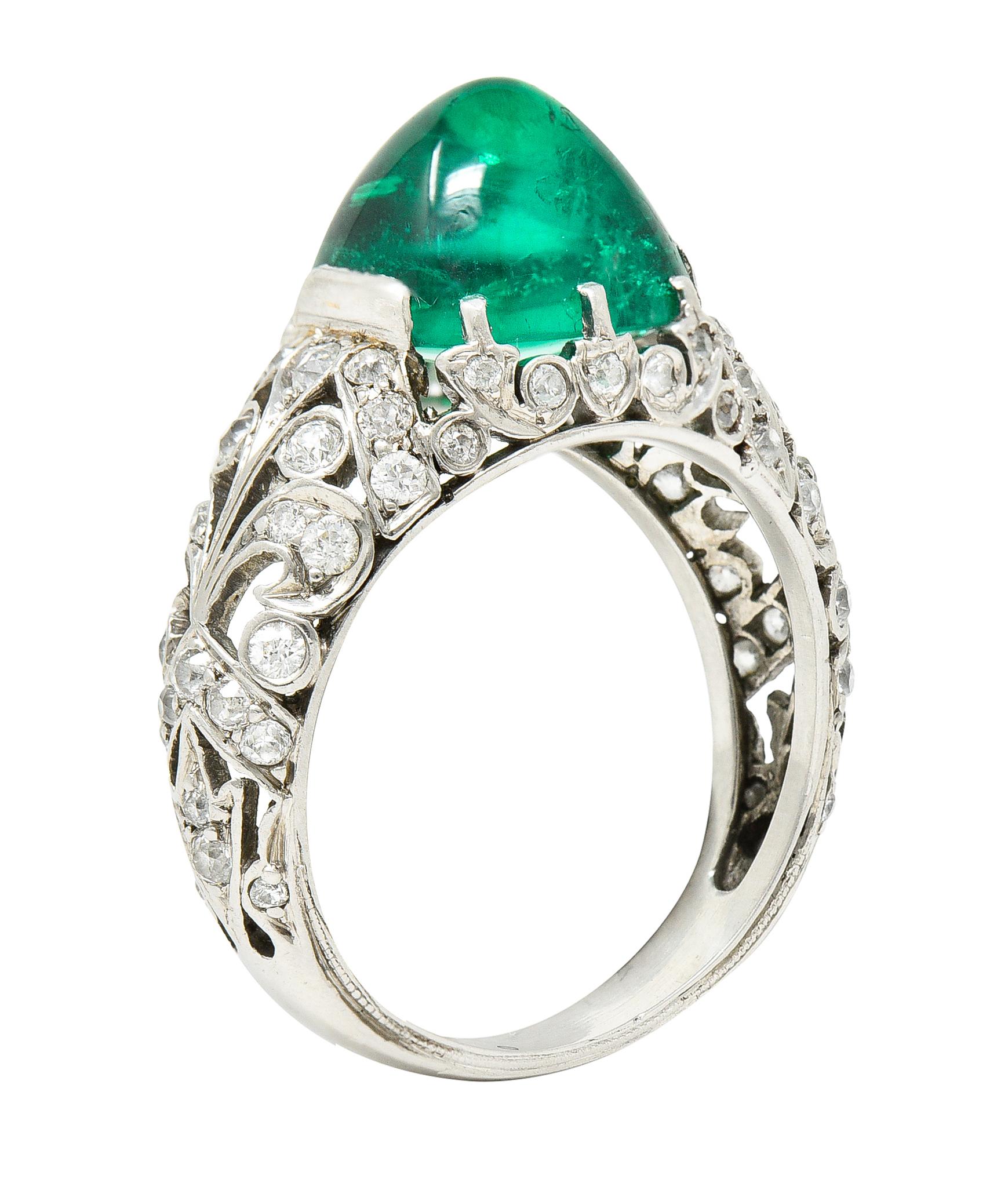 Centering a sugarloaf shaped emerald cabochon - transparent medium green in color. Natural Columbian in origin with minor traditional clarity enhancement. Weighing approximately 4.32 carats total. Prong and tab set with a pierced gallery surround.