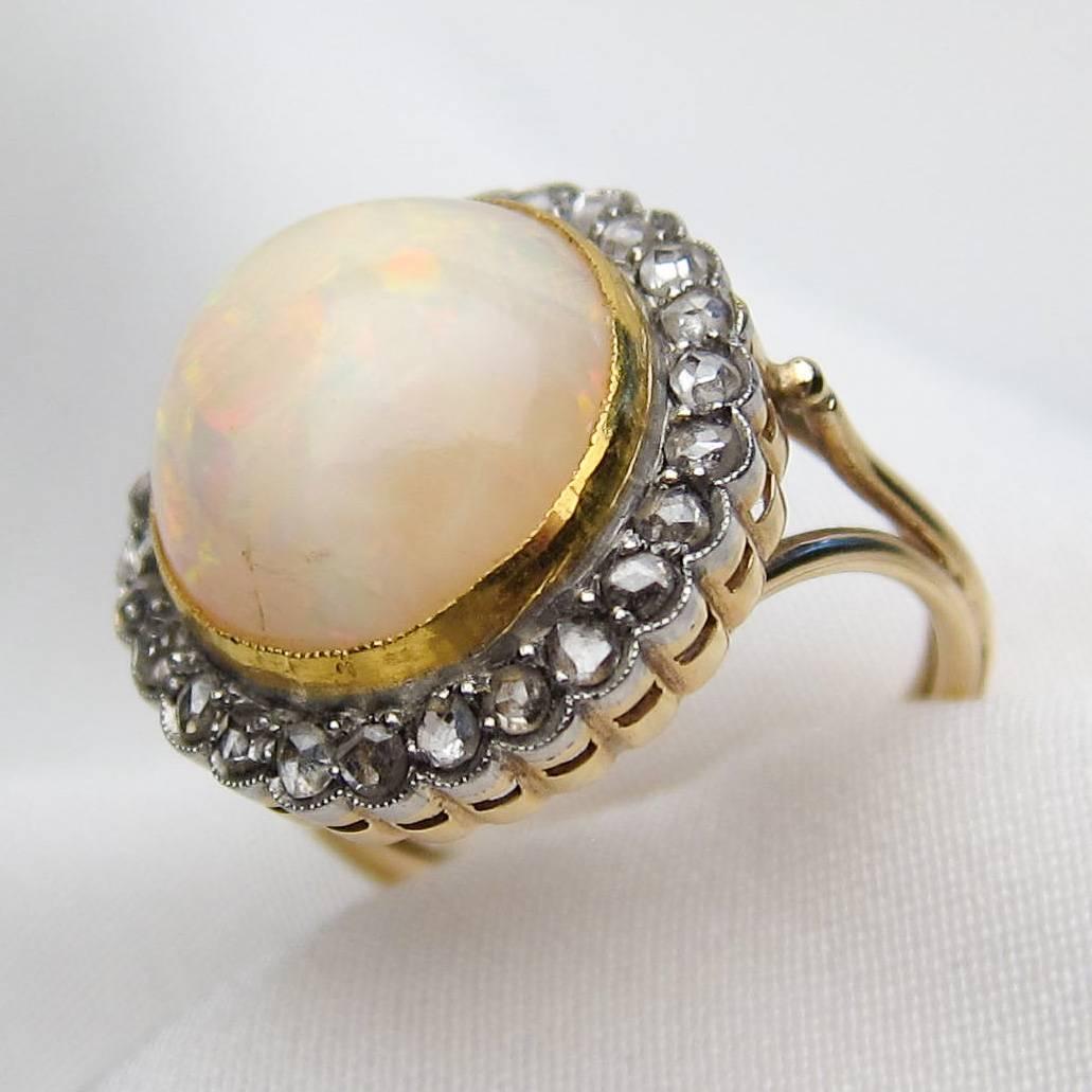 Circa 1910. This beautiful Edwardian platinum-topped 14KT yellow gold ring features a stunning 8.00 carat bezel-set cabochon white opal, displaying a gorgeous green and orange play of color. 26 rose-cut diamonds accent this lovely center stone. The