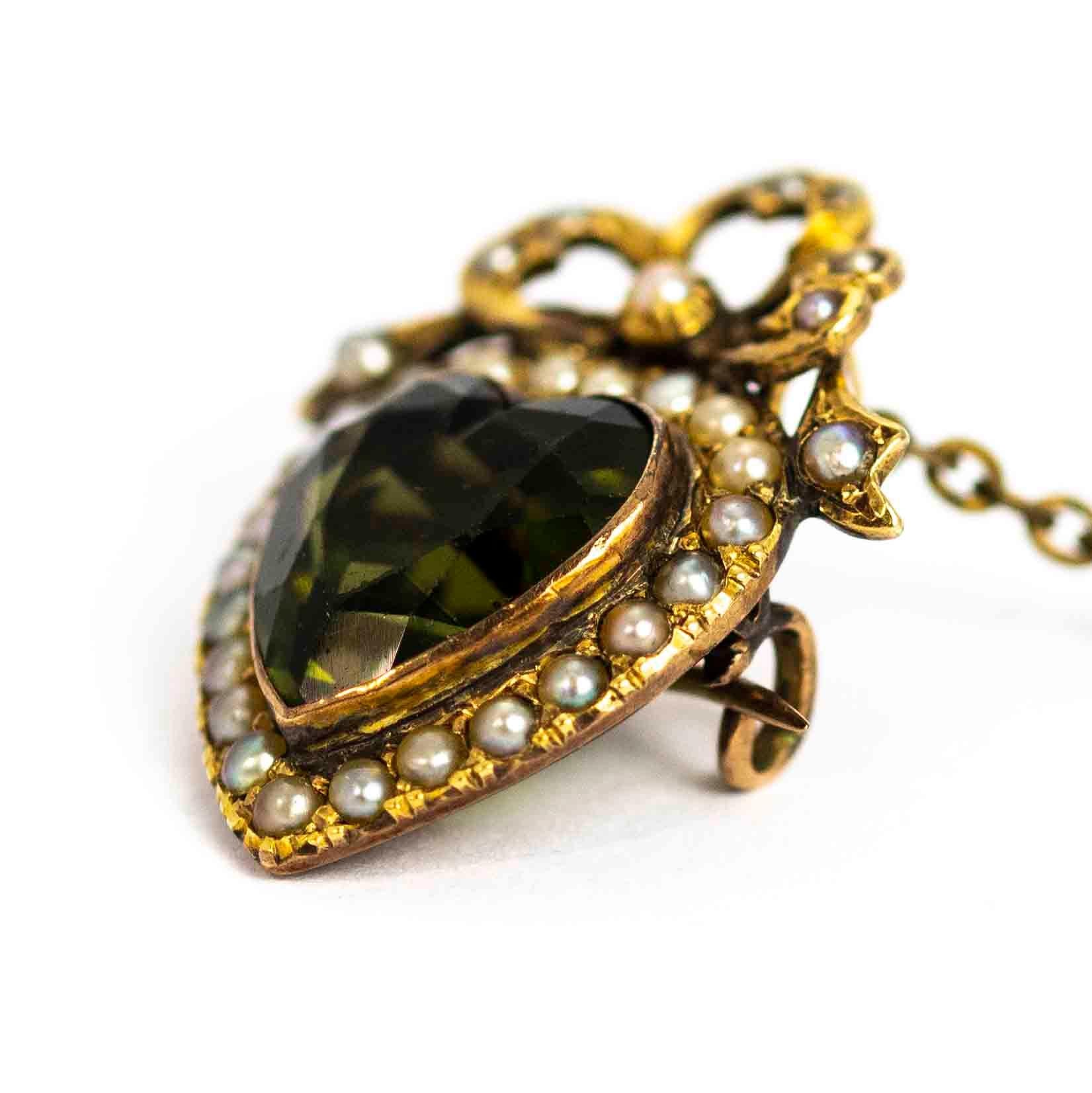 A superb antique Edwardian heart brooch. Centrally set with a heart-cut dark green paste surrounded by beautiful seed pearls. The brooch is topped with a beautiful bow motif inlaid with seed pearls. Modelled in 9 carat yellow gold.

Dimensions: 35mm