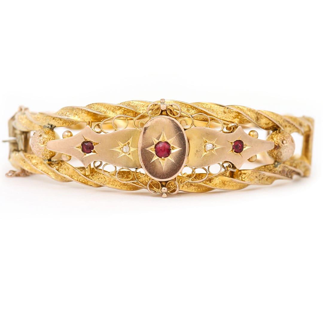 An ornate Edwardian 9ct yellow gold red ruby and diamond bangle. In lovely condition the bangle at its head boasts a carved gold panel with star set rubies and small diamond chips that are surrounded by delicate cursive gold work, flanked either