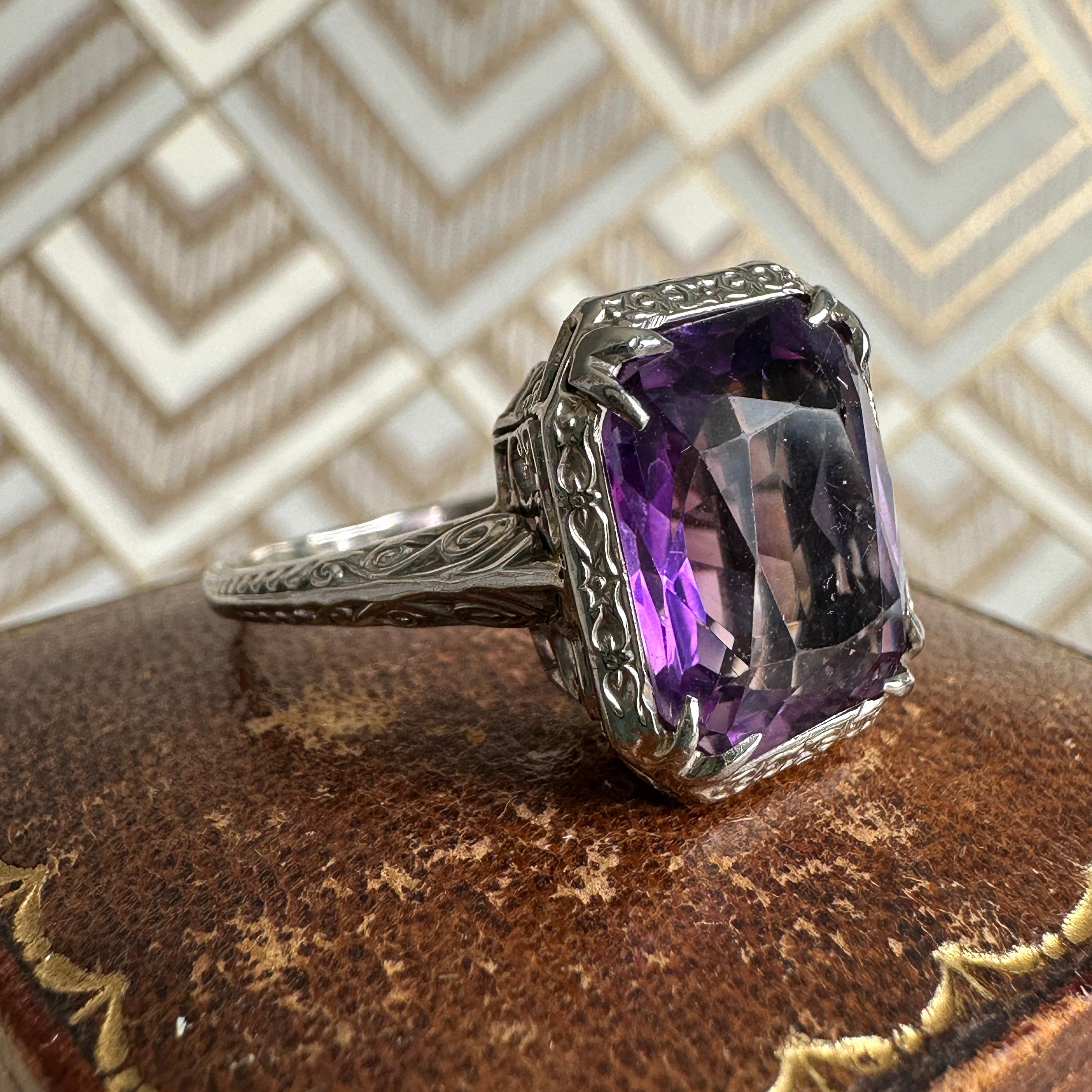 Details:
Sweet Edwardian Amethyst ring in 14K White Gold. The amethyst is a rich deep purple color, with lots of depth. Delicate filigree pattern sets up and frames the stone, with lovely engraving down the shanks. The bezel setting has pretty