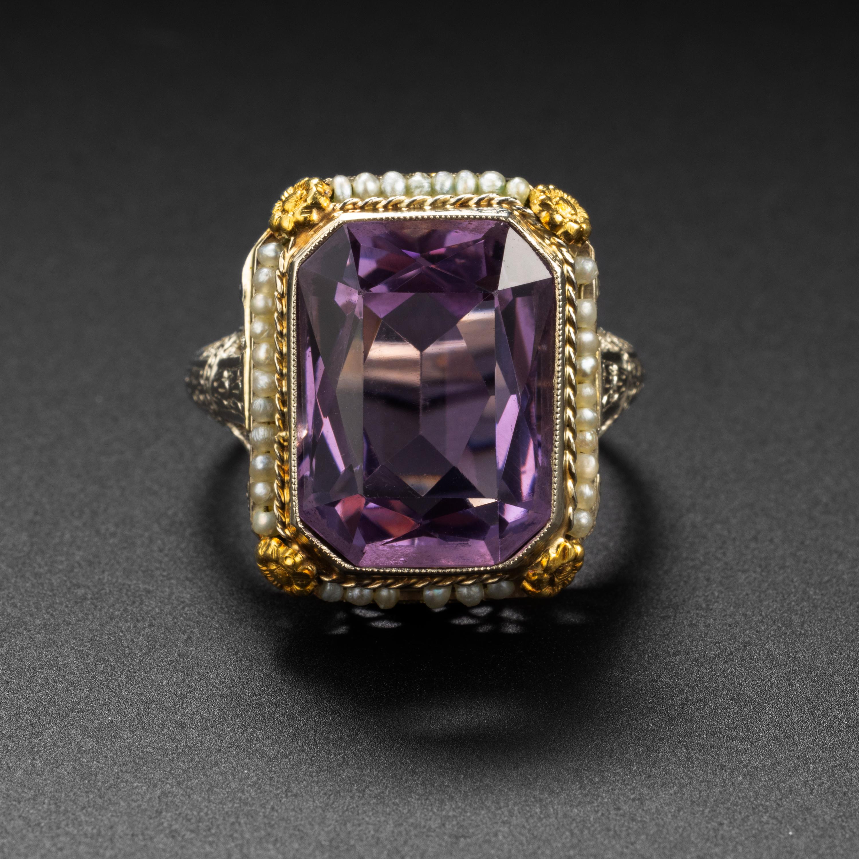 This Edwardian-era amethyst and natural pearl ring features a 15.25 x 12.91mm rectangular-cut natural amethyst of medium tone, bezel-set within an ornate, hand-crafted 14K white and yellow gold mounting and surrounded by a frame of tiny natural