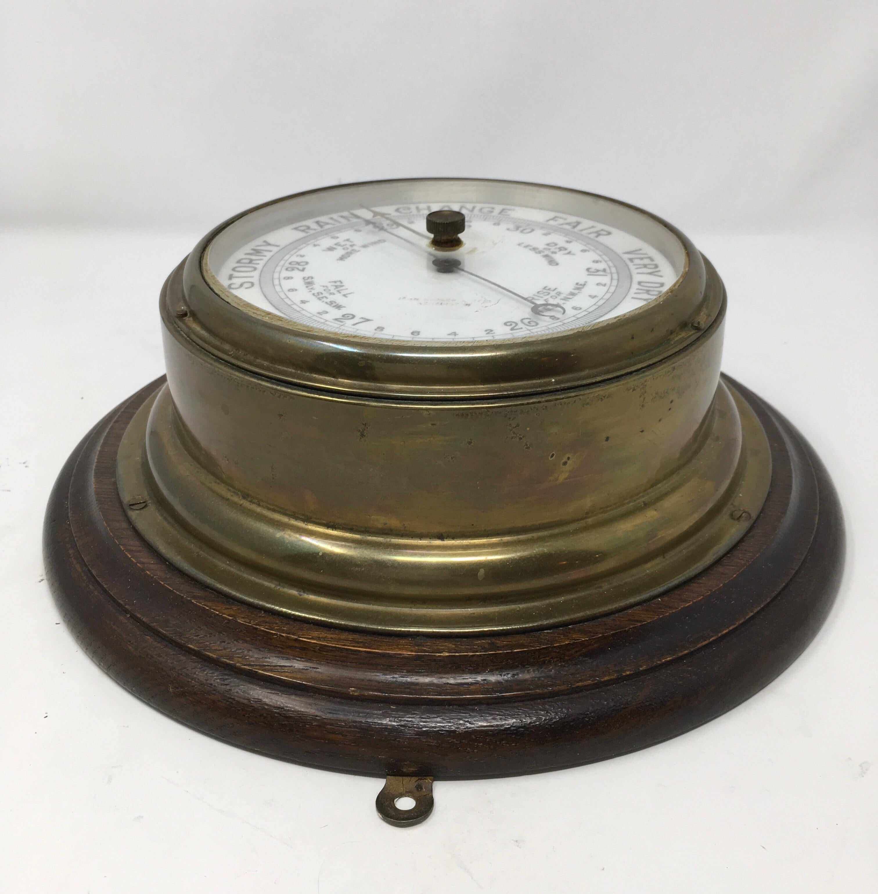 An Edwardian aneroid ships barometer by John Barker & Co LTD Kensington. The barometer is brass cased and mounted on an original oak surround and has bevelled glass to the dial. The dial is faintly marked 'John Barker & Co Ltd, Kensington', circa