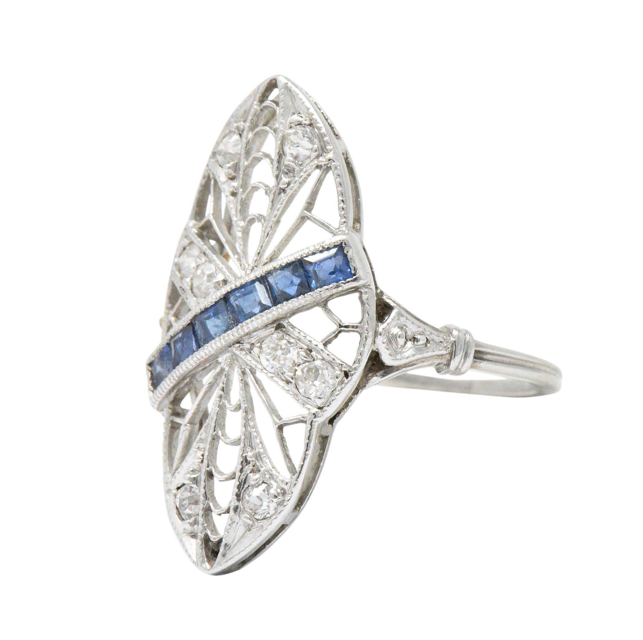 Dinner style ring with an intricately pierced navette form, milgrain detail, and a grooved shank

Bisected diagonally by channel set square calibré cut sapphire that weigh approximately 0.30 carat total; bright blue in color

Accented by Swiss cut
