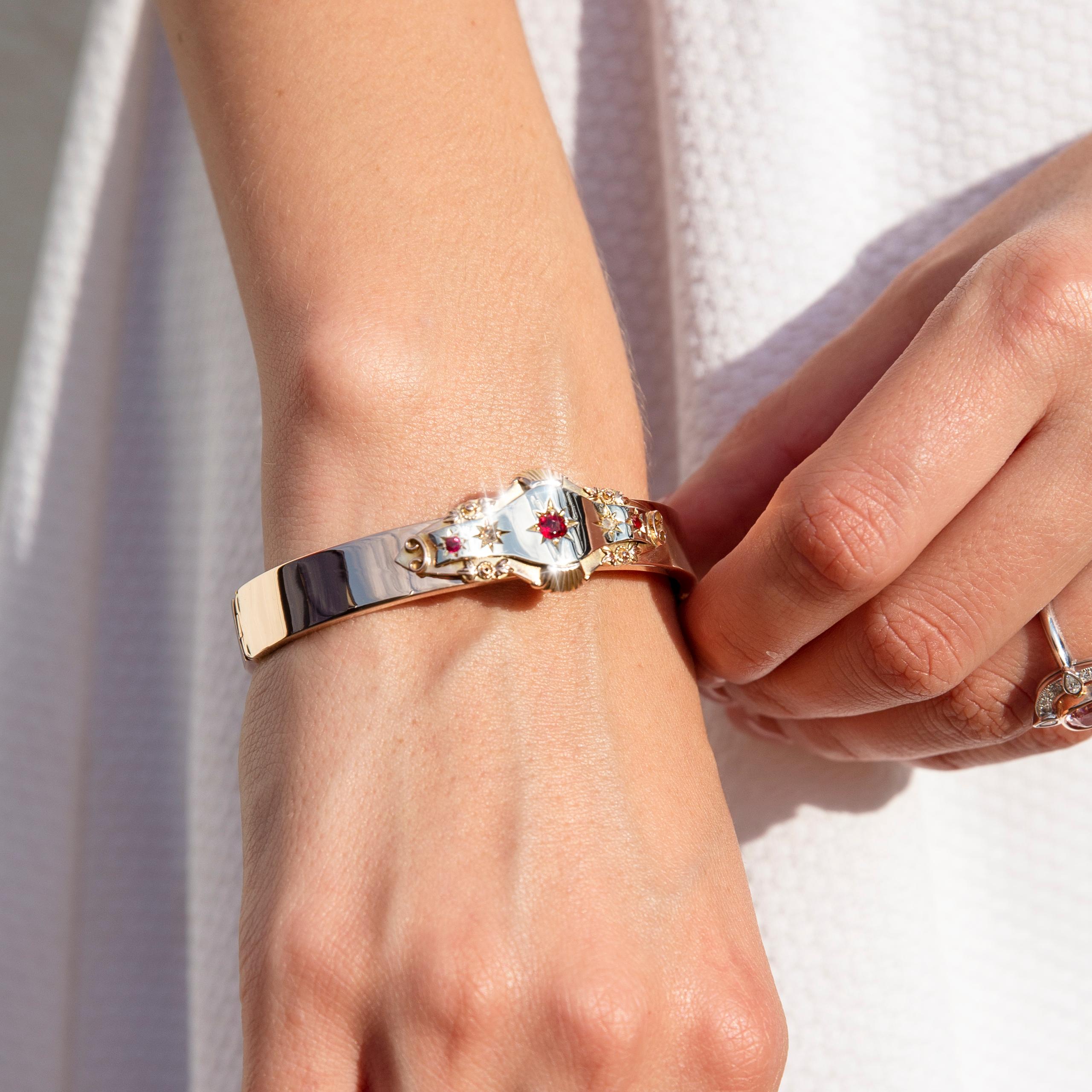 Crafted in 9 carat rose gold, this whimsical Edwardian hinged bangle, circa 1990s, features an alluring deep red gems flanked by a duo of smaller red gems and a further duo of rose cut diamonds. We have named this antique adornment The Maverick