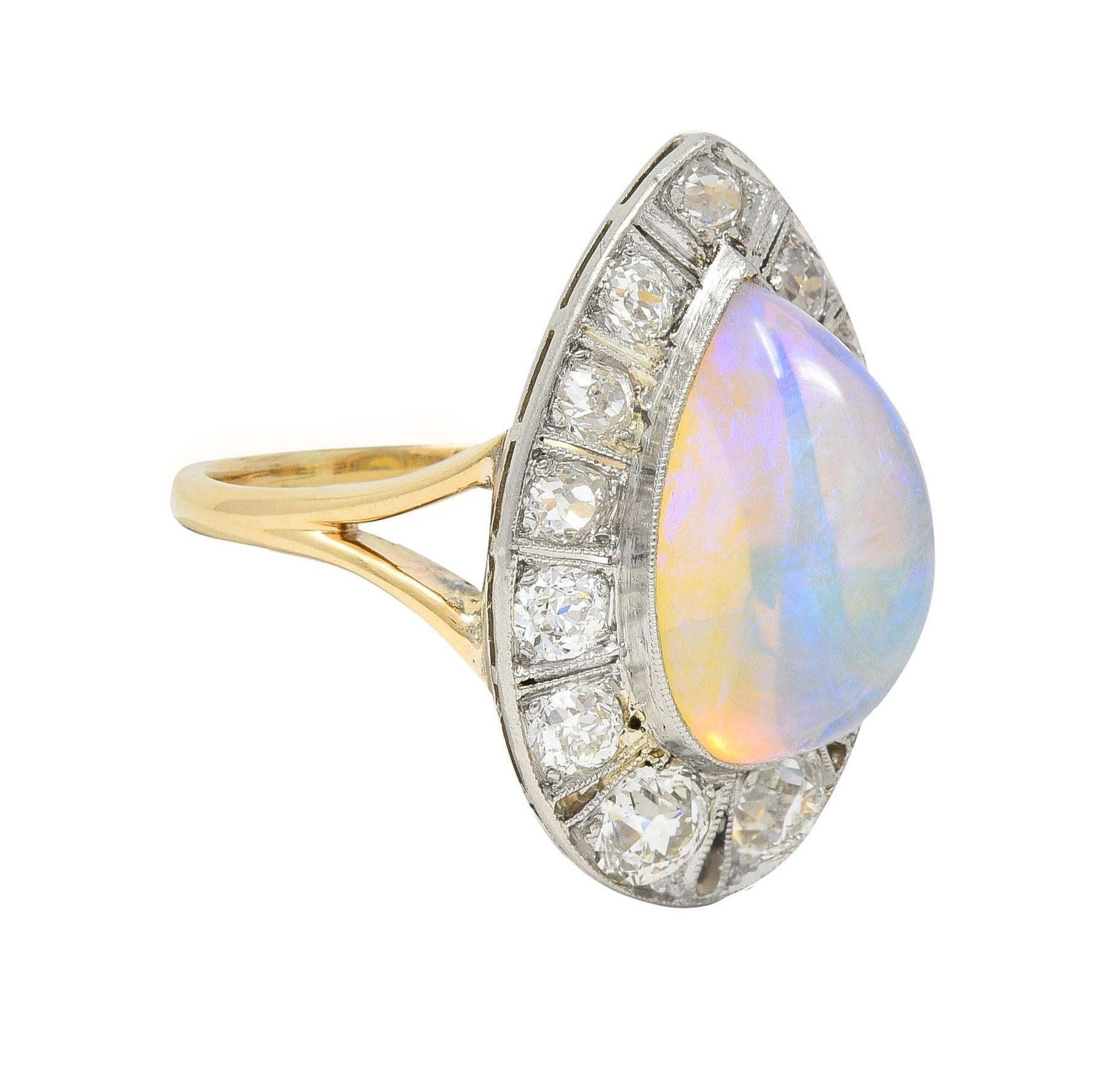 Centering a pear-shaped jelly opal cabochon measuring 8.0 x 13.0 mm 
Translucent colorless body with violet and yellow play-of-color
Set with a platinum bezel with a pierced halo surround 
Bead set with old European cut diamonds 
Weighing