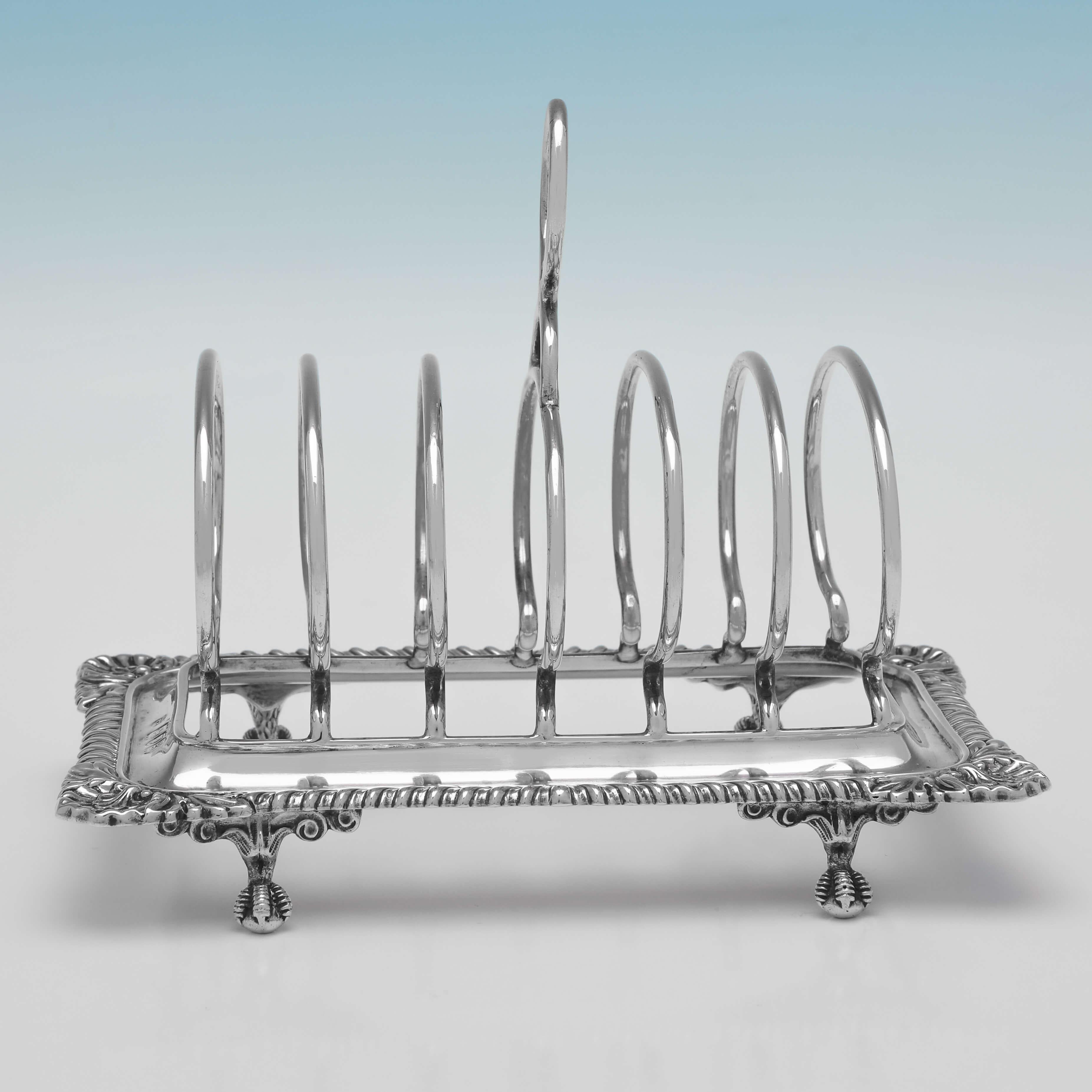 Hallmarked in London in 1902 by Thomas Bradbury & Sons, this attractive, Edwardian, antique sterling silver toast rack, will hold 6 pieces of toast, and features a shell and gadroon border, and ball & claw feet. 

The toast rack measures 5